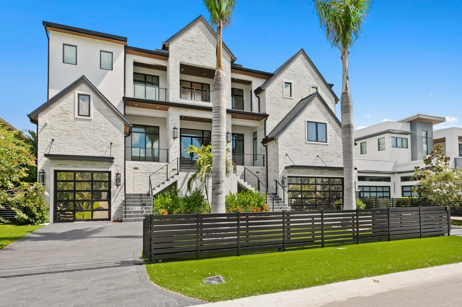 This breathtaking 2024 built gated waterfront estate in coveted Sunset Park reimagines modern coastal living and dramatic bay views just four properties from open water. Built by Brookshire Homes and featuring over $700,000 in custom designer upgrades since purchase, this one-of-a-kind Coastal Contemporary showcases exceptional craftsmanship and custom detail throughout. Built on pilings with block construction, impact windows, and elevated over garage this elevated home offers strength, stability, and peace of mind. From soaring 22-foot foyer to the 10-foot ceilings on both levels, and balconies that frame Tampa Bay’s breathtaking sunsets, the residence has been artfully conceived to balance elegance and livability. Step inside to discover a dramatic display of four opulent crystal chandeliers, wide-plank wood flooring, marble countertops, custom built-in cabinetry, stone feature walls, a convenient 3-stop elevator. A state-of-the-art innovative in-home automation system featuring Control4 technology, automated blinds, Lutron smart lighting, and WiFi-enabled integration throughout. The home’s versatile open floor plan features a large great room with a gas fireplace, office, a first-floor laundry and mud room, and a chef’s kitchen with top-of-the-line Thermador appliances, a plumbed coffee station, dual dishwashers, multiple beverage refrigerators, and a walk-in pantry. The expansive media room includes a built-in bar, immersive lighting, and a full bath that also serves the outdoor entertaining space, creating a dynamic setting for gatherings and entertainment. Upstairs, the primary suite exudes unparalleled luxury, complete with a retractable screen, a dramatic marble feature wall, an elevated platform to capture sweeping water views, and a spa-inspired bathroom with a steam shower designed for luxury. A custom-designed glam bedroom suite offers illuminated mirrors, custom display cabinetry, and its own spa-like full bathroom for the ultimate boutique-style experience. Three additional en-suite bedrooms with walk-in closets, a loft with wet bar and purified water station, and a secondary laundry room complete the upstairs level. Outside, a true resort-style oasis awaits with a full alfresco kitchen complete with pizza oven, gas grill, sink, and beverage fridge, a covered lanai with tongue-and-groove ceilings and retractable outdoor screen, and a spectacular pool with waterfalls overlooking the Bay. The property further features a covered composite dock with boat lift for boating access to Tampa Bay, generator and a garage with capacity for approximately 6 vehicles enhanced by custom epoxy flooring. With boating access to Tampa Bay and the Gulf, and just minutes from Tampa’s vibrant urban core and the cultural sophistication of downtown St. Petersburg, this residence offers the ultimate waterfront lifestyle for the most discerning buyer. Available furnished at additional cost.
