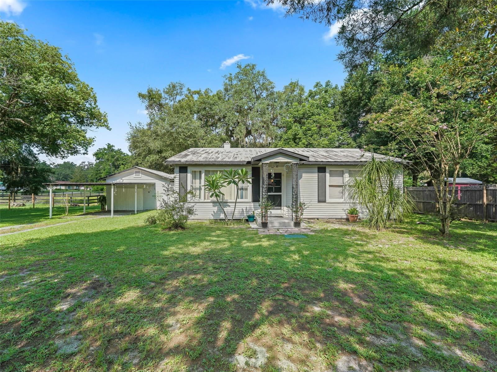 Discover the perfect blend of old Florida charm and modern comfort in this adorable vintage Cracker-style home nestled on a generous .48-ACRE lot in the heart of Wildwood. Step inside to find large, welcoming rooms with an open-plan living area that creates the perfect balance of cozy and spacious. The heart of the home showcases a stunning farmhouse-style kitchen featuring elegant GRANITE COUNTERTOPS and a unique rolling island crafted with distressed whitewash wood—ideal for meal prep and entertaining. The sink sits perfectly positioned beneath a huge window, flooding the space with natural light. The thoughtful layout includes a spacious dining room and large living room, perfect for both everyday living and hosting guests. Two generously sized bedrooms provide comfortable retreats, while the well-appointed bathroom completes the interior. A delightful screened porch/breezeway seamlessly connects the main home to a practical workshop/laundry room, extending your living space while maintaining the authentic Florida lifestyle. The front carport offers convenient protection for your vehicle from sun and storms. The true treasure of this property is the HUGE FENCED BACKYARD, dominated by a magnificent granddaddy oak tree that provides abundant shade and creates a naturally beautiful, comfortable outdoor retreat year-round. Practical touches include a double gate opening to 2nd Avenue, offering excellent access for parking your trailer, camper, boat, or recreational vehicles. Located just under 2 miles from Brownwood Paddock Square, you'll enjoy easy access to nightly entertainment, shopping, and dining, plus the beloved Saturday farmer's market. This unique property offers the rare opportunity to own a piece of authentic Florida history while enjoying modern amenities and an unbeatable location.