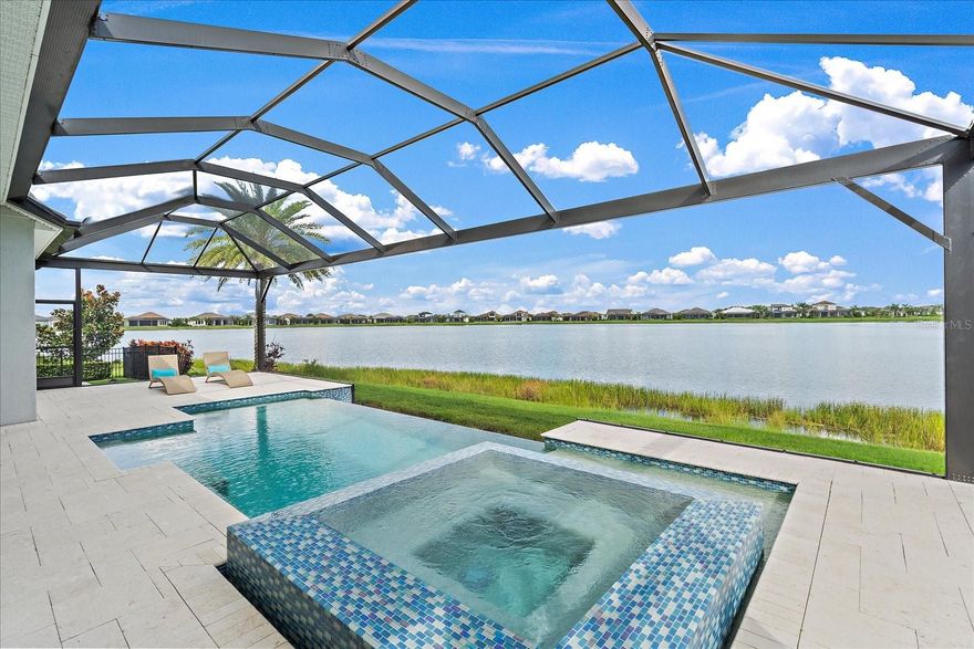It simply does not get better than this turnkey furnished Tideland model in Waterside’s Lakehouse Cove.  This pristine home features all of the upgrades of a model and more, all situated on a gracious lakefront lot with a stunning & unparalleled water view right from the front door.  You'll be wowed from the moment you walk in by the infinity pool and spectacular view of the expansive lake beyond.  One of the most notable upgrades is that the home was raised to allow for the most dramatic view and a seamless visual connection between the pool and water, with panoramic screens for maximal enjoyment. Inside, LED-lit tray ceilings & crown molding, plus modern designer light fixtures, furnishings, and decor throughout complete this perfect picture. The great room is a showstopper with custom built-ins & architectural detailing surrounding an electric fireplace that sets the tone for the level of elegance throughout the home.  Functionality meets design in the chef's kitchen with an abundance of solid wood cabinetry, designer hardware, large central island, quartz counters, extra-large farmhouse sink, under cabinet LED lighting, subway tile backsplash, walk-in pantry, and butler pantry. The first level also encompasses a den/office overlooking the sparkling lake and a guest suite, as well as a powder bath. Moving upstairs, owners & guests alike will love the large bonus room and dry bar, and everyone will also enjoy the privacy and functionality provided by the adjacent third bedroom & bath. Nature abounds with water views over tropical palm trees waving in the breeze from upstairs, and an incredibly spacious expanded travertine lanai with room for everyone.  From the fully equipped outdoor kitchen to the fire table and upscale loungers & seating, it is the perfect blend of luxury and functionality. Lakehouse Cove has a 7-acre amenity center that includes a resort-style pool, a kayak boat house, a fitness center, a club house, pickleball courts, bocce ball courts, a dog park and an event lawn. Waterside Place features dining, shops, activities, and the highly-rated Sunday Farmer’s Market, and you are also just minutes from the Sarasota Polo Club, freeway access, and all of the amenities offered at Lakewood Ranch’s Main Street & also University Town Center.  The pristine beaches of Siesta, Lido, and Longboat Key await just a short drive away too. There is nothing left to be desired here…your new home in paradise is ready!