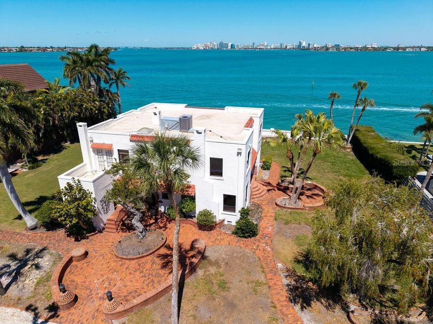 Tucked away on highly sought-after Bay Island, just over the North Siesta Key Bridge, 679 Norsota Way is a rare opportunity to own a piece of Sarasota’s architectural history or create something entirely new. Built in 1926, this Mediterranean Revival Spanish Colonial estate sits gracefully on an expansive 2/3-acre lot, offering timeless character, generous scale, and unmatched potential. The property is one of the largest parcels on Bay Island with 150 feet of deep water bayfront, presenting a rare offering for a new waterfront estate with perhaps the most coveted view in Sarasota.
The existing 3,788 sqft two-story residence captures breathtaking views overlooking Sarasota Bay, the Ringling Bridge, and the downtown skyline, a daily backdrop that defines true coastal living.
Importantly, the property is not historically designated, presenting a high level of flexibility. For those seeking new construction, this exceptional 2/3-acre homesite offers the opportunity to start fresh without the constraints of an HOA or significant building restrictions, an increasingly uncommon advantage in such a premier location. No deed restrictions or grand oaks constrain future construction. Perfectly positioned just 10 minutes to downtown Sarasota and 5 minutes to the beach, this property blends privacy, proximity, and prestige in one of the area’s most coveted neighborhoods.