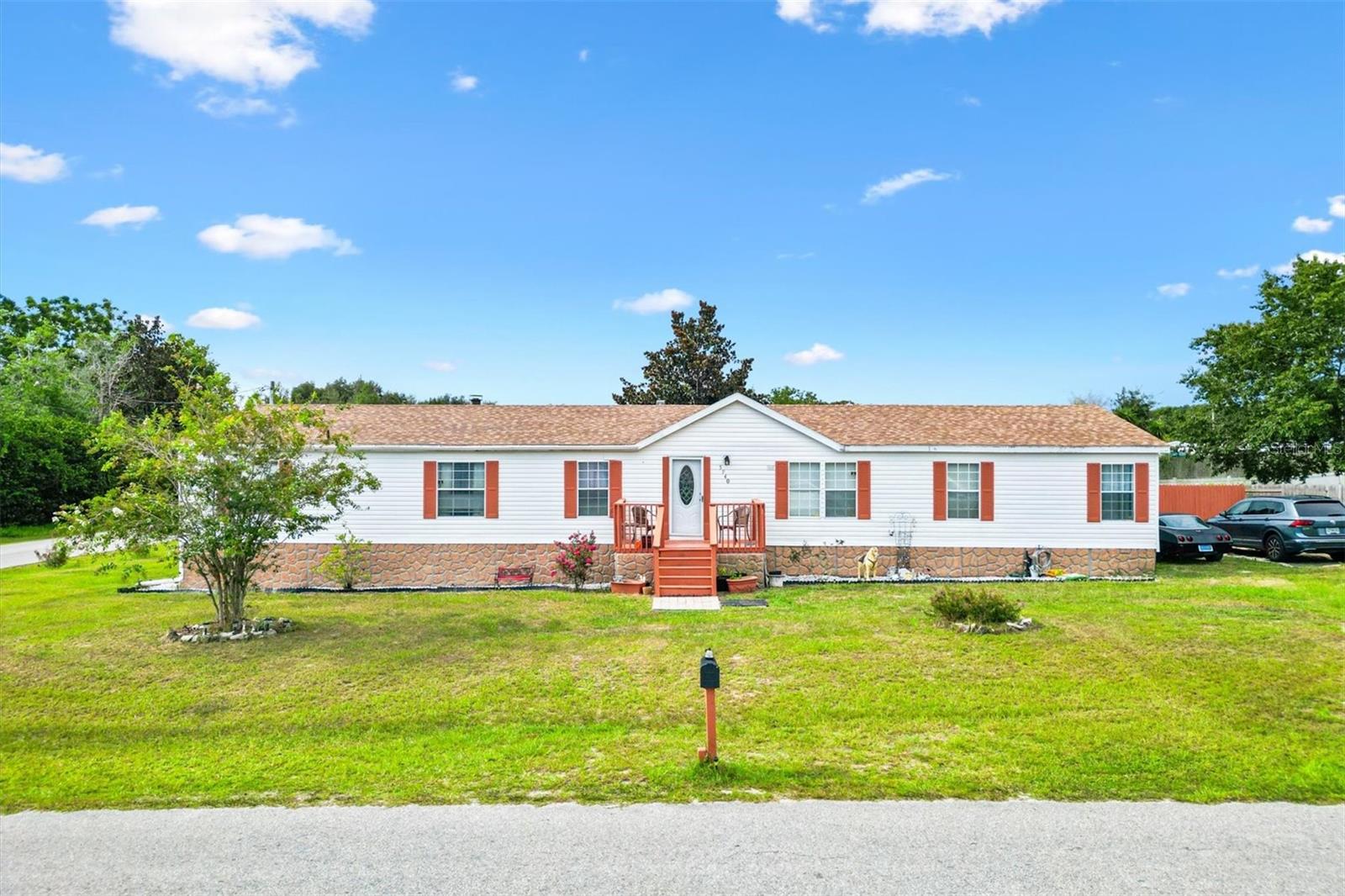 5 bed 3 bath double-wide manufactured home on a corner lot in Bellview Hills Estates. This location can’t be beat with access to hwy 301, a great connector heading north to Ocala and south to Summerfield and the Villages. Close to grocery stores, shopping, hospitals, and schools.
This home features a split floor plan in 1,976 sq. ft. of indoor living. Step inside to a carpeted living room with ceiling fan, adjacent dining room, and a carpeted family room featuring a cozy wood-burning fireplace. From the dining room, sliding doors lead to a wood deck overlooking the backyard, ideal for entertaining or enjoying a quiet morning coffee. The large open kitchen is equipped with stainless steel appliances and provides plenty of room for cooking and gathering. With four bedrooms and two well-appointed bathrooms on one side of the home, including a convenient Jack and Jill bath connecting two bedrooms with a dual vanity and tub, this layout is perfect for families. The spacious master suite off the living room offers a walk-in closet and a private bath with soaking tub, walk-in shower, and vanity. Outside, the large fenced backyard offers a private oasis for recreation, pets, or gardening, making it the perfect spot to unwind and enjoy the outdoors. Don’t miss the chance to make this beautiful home yours! 2025 Roof, water filtration system