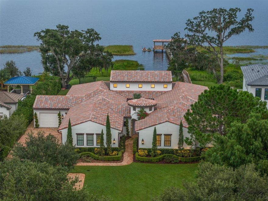 One or more photo(s) has been virtually staged. Welcome home to this stunning single-story, Santa Barbara-style custom residence on the serene shores of Lake Hart, within the gated North Shore golf community. Blending Mediterranean elegance with California rustic charm, the home is surrounded by conservation land and protected state park shoreline, offering both privacy and a true resort-style lifestyle. Built with meticulous attention to detail, this 5,139 sq. ft. energy-efficient home features five bedrooms, four and a half baths, a bonus room, and an interior courtyard. The open floor plan is anchored by a newly renovated gourmet kitchen and great room, each designed to highlight breathtaking lake and pool views. The kitchen showcases premium cabinetry, an oversized island, and a stylish bar area with sink, refrigerator, wine storage, and glass racks—perfect for entertaining.
The primary suite is a private retreat with sweeping lake views, a fireplace, sitting area, dual walk-in closets, and a spa-like bath with a spacious walk-in shower. Additional living spaces include a formal dining room, study, and a bonus room with fireplace that flows seamlessly to the outdoor living area. Step outside to your private oasis, complete with a resort-style pool and spa, outdoor summer kitchen, Sonos surround sound, and upgraded finishes throughout. The backyard also features a covered boat dock with electric hoist, ideal for water sports, fishing, or simply enjoying the sunset over Lake Hart. Unique wood beams sourced from the property add character throughout the home.
Practical luxury continues with a 4-car garage, including one of the garage spaces that has been transformed into an air-conditioned home gym, easily convertible back to vehicle storage if desired. Custom storage throughout the garage provides additional functionality and organization. Conveniently located just minutes from Lake Nona’s Medical City, Boxi Park, the USTA National Campus, top-rated schools, and Orlando International Airport, this home delivers a perfect blend of private resort living with city conveniences. North Shore is anchored by a premier 18-hole championship golf course, elevating the lifestyle in one of Orlando’s most desirable communiti