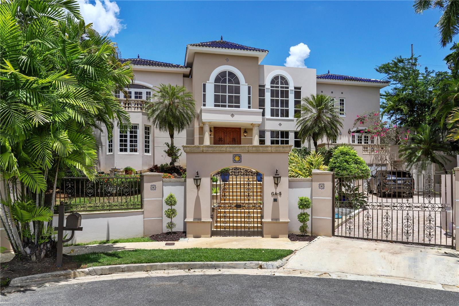 Contemporary-style custom-built residence, situated on a tranquil cul-de-sac street within Garden Hills, one of Guaynabo's most esteemed neighborhoods. Nestled on a 1,434 square meter lot within a gated community, this spacious home encompasses 6,780 square feet of living space.
Boasting meticulous craftsmanship and thoughtful design, this two-story dwelling showcases a captivating grand foyer entrance adorned with soaring double-height ceilings. Its refined interior comprises an ample living room, formal dining area, media room, family room, home office, fully equipped kitchen with breakfast nook, laundry, and maid's quarters. The generous accommodation encompasses five splendid bedroom suites, each featuring en-suite bathrooms and walk-in closets, alongside six full bathrooms and one powder bath.
Designed with attention to detail, this residence impresses with an array of exceptional amenities great for family living or for entertainment. A wine cellar with a capacity for 500 bottles. A delightful outdoor terrace invites relaxation, while a spacious patio adorned with fruit trees offers an idyllic retreat. The property further boasts a gazebo great for grilling, a sparkling pool, and a rejuvenating Jacuzzi, perfect for indulging in leisurely moments. Other features include cathedral ceilings, security windows and doors, a 1,000-gallon water cistern, and a 35-kilowatt diesel backup generator.
Conveniently located near the best schools, restaurants, shopping and only approx. 15 minutes away from San Juan.