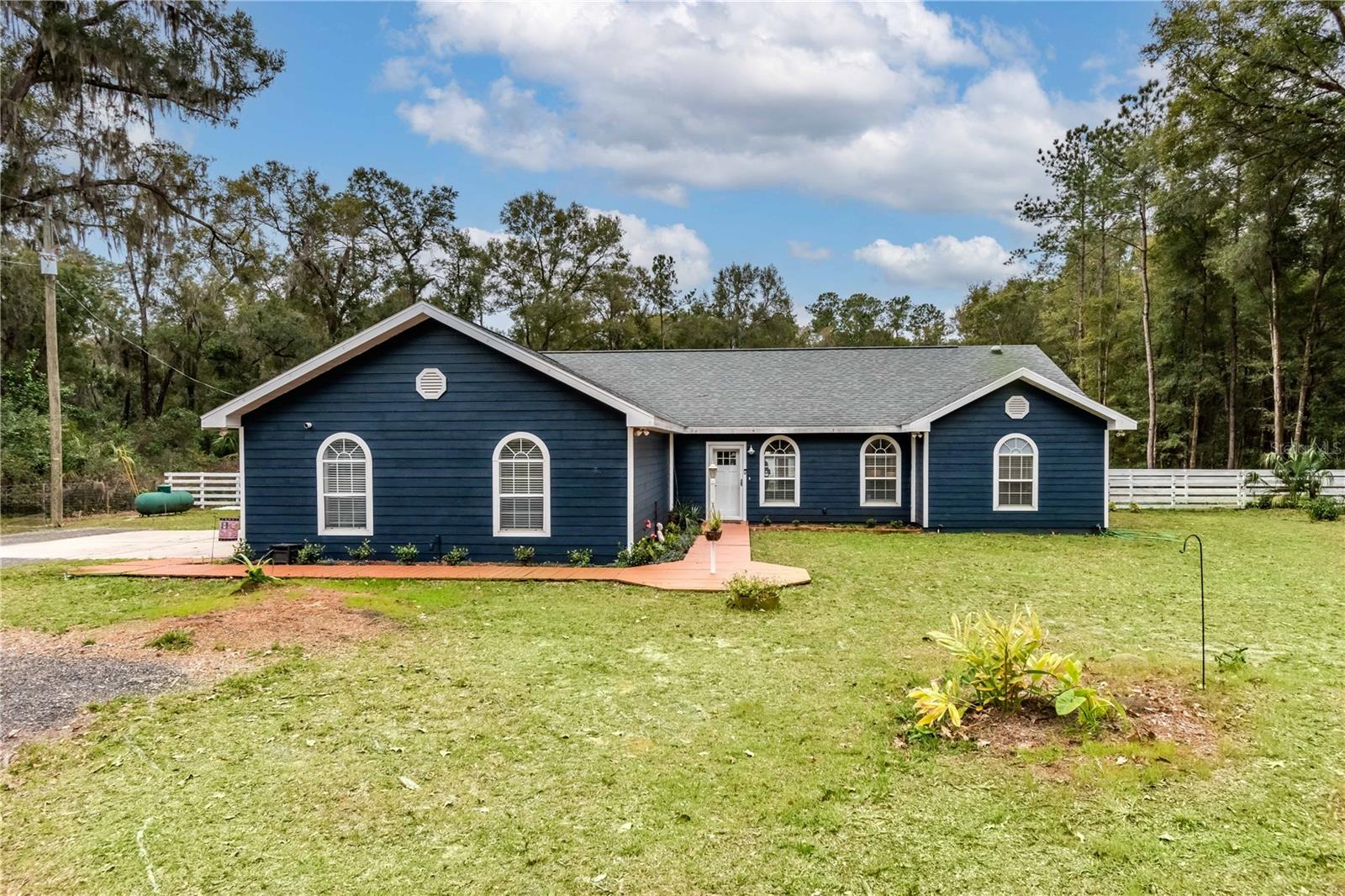 Situated on 2.85 acres, this newly remodeled home offers plenty of updates and a quiet but convenient location! Set back from the road for added privacy and gently shaded by mature trees, the home features a fresh coat of paint, new roof, thoughtful landscaping, and a wooden walkway that offers plenty of curb appeal. Offering a total of 3-bedrooms and 2-baths, the home features high ceilings and a split-bedroom floor plan that adds plenty of privacy to the primary bedroom. New porcelain tile runs throughout the main spaces of the home for ease of clean-up, and new barn doors have been set-up in the formal dining area and at the entrance to the guest area. Nicely open, the main spaces have a well-thought out layout that allows for flowing conversation throughout the living, dining, and kitchen areas. All bedrooms feature newly installed Luxury Vinyl flooring for a sophisticated finish, and each bedroom has also recently been remodeled. Especially inviting is the primary bedroom, which offers a larger layout, walk-in closet, and a private en-suite bathroom that includes dual vanities, jetted tub/shower combo, and a glass-door shower. At the back of the home is a large patio with fencing and a gate that provides plenty of space for seating and entertaining, all directly overlooking the large, open backyard. A detached building has ample opportunity for use as an in-law suite, guest accommodations, or a private office if desired with freshly added drywall, electric, and plumbing. A Generac Generator and 500 gallon propane tank keep the power up and running in case of storms, and there are three 50 amp RV plugs on property– one on each side of the house and another on the detached building. The entire perimeter of the property is fenced for added security, and an additional section attached to the porch has been fenced off for use as a dog-run. Horses allowed with special use permit. This property is highly convenient, with Publix just two miles away from the property and the Downtown Ocala Square just 10 minutes away for a variety of shopping, dining, entertainment, and medical options! With a prime location that blends extensive updates, convenient location, and plenty of privacy, this thoughtfully updated-for home is an inviting option for those looking to get the most out of Ocala!