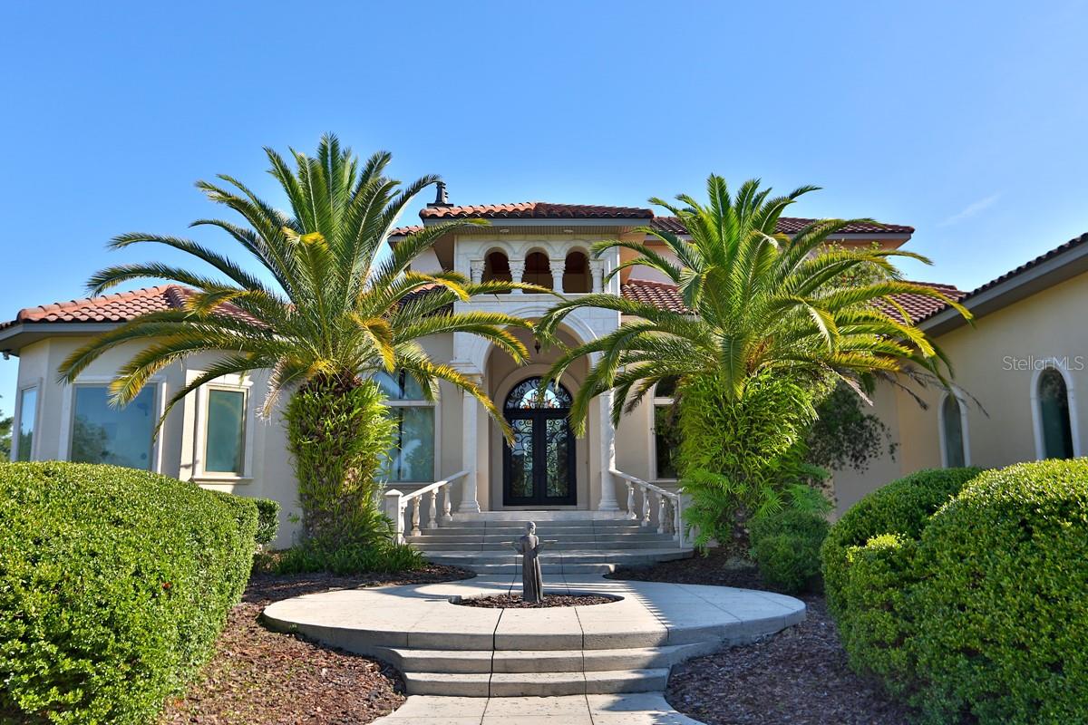 Impeccable attention to detail, masterful construction, and a prime location makes this two-story Mediterranean-style estate on 2.7+/- acres in Ocala a true masterpiece. The grandeur of this property is evident from the first step through the wrought iron double doors adorned with exquisite scrollwork. The 26-foot ceiling in the living room, complemented by a bespoke fireplace and a stunning hand-made staircase, creates an atmosphere of elegance. Dark, rich hand scraped hard wood floors. French doors open to a picturesque patio flanked by Corinthian-style columns, perfect for outdoor relaxation.
The heart of the home, the kitchen, boasts travertine floors, custom cabinetry, granite countertops, and top-of-the-line appliances. Seamlessly connected to the dining and living areas, it is an ideal space for entertainment. The kitchen also hosts a morning room & sit-in bar between the family room & kitchen. A spacious walk-in pantry is adjacent to the kitchen, with floor-to-ceiling shelves. Wet bar with a wine fridge & ice maker.
The spacious office/den, adorned with custom cabinets, is a versatile room for various purposes. This home also features a spacious patio, an elegant dining room, a playroom, and an open bonus room.
The owner's suite is a luxurious retreat with dual closets, a sitting area, and a spa-like bath featuring a double-entry walk-through shower, garden tub, and double vanities. On the opposite side of the house, two oversized bedrooms each offer a walk-in closet and a private lavish bath.
Ascending to the upper level, you'll will find an entertainment hub or an additional private living space with a bedroom and bath, offering expansive windows with beautiful outdoor views. This room could efficiently serve as a theater, man cave, or extra private living space. There is a bar area with custom cabinets, an ice maker, and an impressive bar-style glass-door refrigerator. Deep, deep brown granite dresses the countertops with a custom edge. An inviting guest bedroom and full bath with chocolate Italian tile round out the upstairs. Both rooms open onto a large balcony.
The estate's stucco exterior with a barrel tile roof, gated entry, and extra amenities such as a security alarm, sprinkler system, and a custom tree house add to its allure. Furthermore, adjacent custom homes and in-law quarters provide the ideal setting for multi-families seeking space and privacy.
Every element of the home was built to the highest standards, and the finished work and detail are unrivaled. Don't miss the opportunity to own this exceptional estate offering impeccable attention to detail, masterful construction, and a prime location."