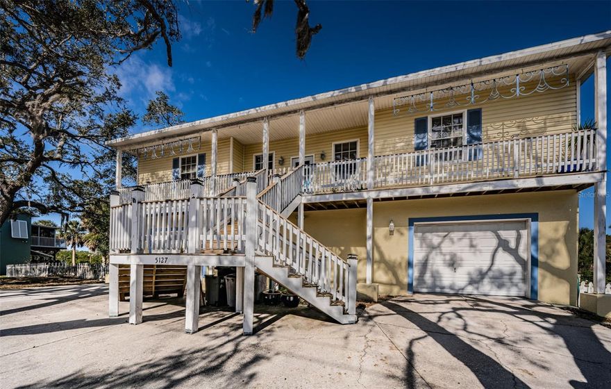 Waterfront Key West–Style Home with Private Boat Ramp, Gulf Access, and Dual Garages | Port Richey, FL 34668
Experience classic Florida waterfront living in this Key West–style home set on .48 acres of waterfront land, framed by mature oaks and coastal scenery. Elevated approximately 13 feet, the home offers the rare combination of water views, outdoor living space, and functional parking/storage all in a golf cart–friendly community with easy access to Downtown New Port Richey and Sims Park. From the moment you arrive, the home’s elevated design and expansive porches create the feeling of “living in a treehouse,” with wide-open skies and a true waterfront backdrop. Waterfront home with a private boat ramp for small crafts, such as kayaks, skiff boats, jet skis, etc. Minutes to the open Gulf of Mexico and waterfront dining less than a mile away. The property has three driveways with boat parking + RV parking on site. Larger boat access via public boat ramp and private marina is less than a mile away. A new roof will be on by closing. The home is built to up-to-date hurricane standards and designed to withstand a Category 3 hurricane.
Interior Layout has an open, bright design and is designed for everyday comfort. The living area offers a highly desirable layout with four bedrooms, an open living room/dining room/kitchen combination, tall ceilings, and an inside large laundry room.  A split floor plan supports privacy, while the large primary bedroom spans the full length of the home, an impressive feature that is difficult to find in this segment of the waterfront market. Flooring includes tile and laminate throughout, ideal for low-maintenance coastal living. Dual Garages + Private Flex Suite (Rare Value-Add) Downstairs features two large garages, plus a highly functional bonus space located between the garages with a private entrance ideal as a mother-in-law suite, gym, guest suite, or potential short-term rental (Airbnb-style) setup.  Enjoy multiple outdoor areas designed to maximize the setting of a true outdoor entertaining space, including an open front porch, a screened-in back porch, and a private deck overlooking the natural waterfront landscape.  Whether you’re entertaining, relaxing, or launching for a day on the water, the lifestyle here is exactly what Florida waterfront buyers are looking for. If you want waterfront access, Gulf proximity, boat/RV parking, and flexible space in one property, this home is a must-see.