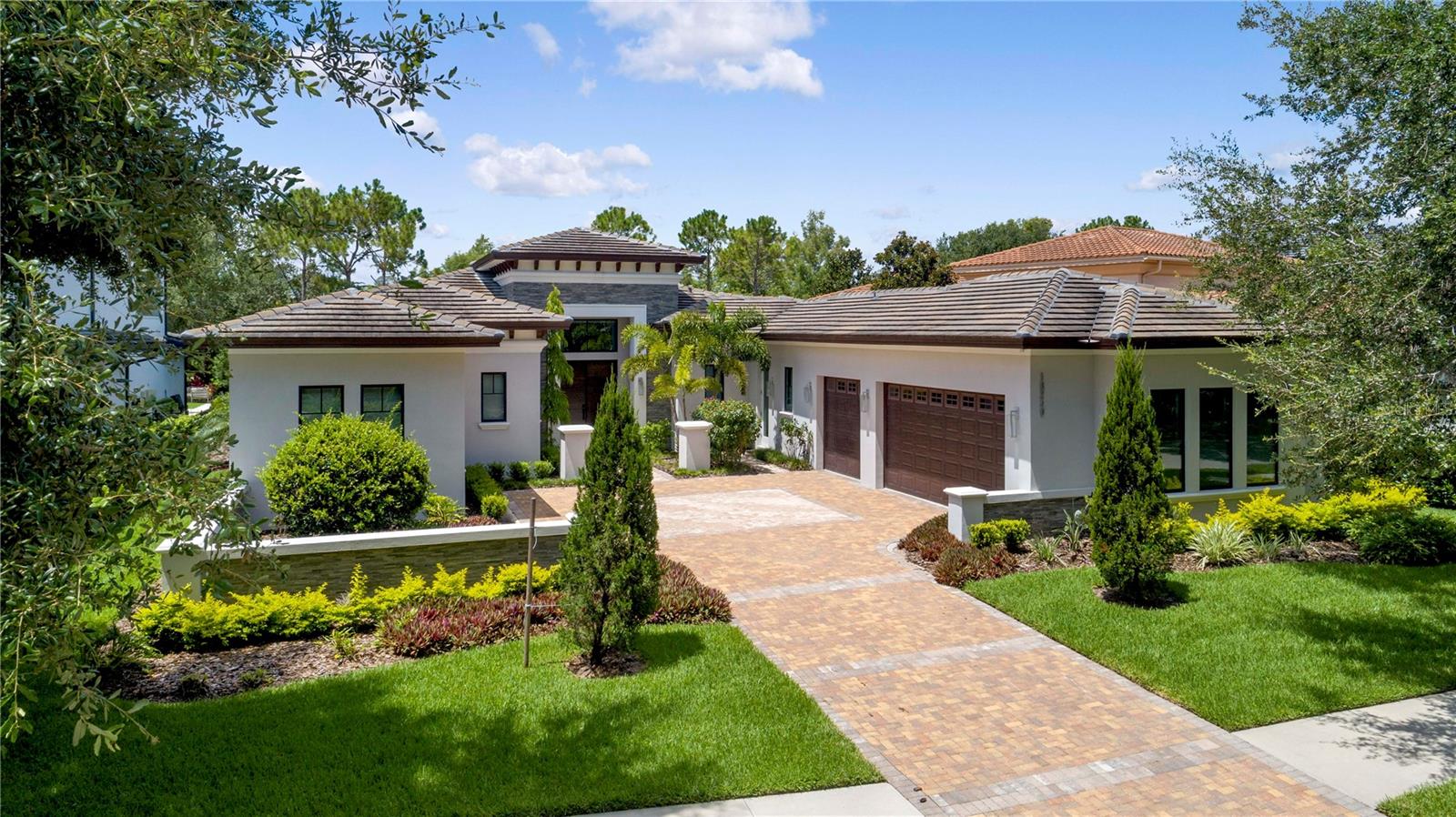 This transitional single-story home, custom built in 2021, offers an open floor plan built for both entertainment and comfortable living. This four-bedroom, four-bathroom residence provides more than 3,300 square feet of interior living space and features an incredible, private outdoor living area with an infinity-edge pool.
White polished porcelain floors stretch throughout the main living areas of the home including the foyer, formal dining area, family room and kitchen. The kitchen displays high-performance appliances by Bosch and Sub-Zero, an elegant coffee bar with wine storage, walk-in pantry, black quartz countertops and a grand center island that adjoins the kitchen and family room.
Floor-to-ceiling sliding glass doors lead from the family room to the large outdoor living area. A stone paver deck extends off the back exterior of the home, connecting the covered lanai with a summer kitchen, sparkling pool with raised spa and sophisticated landscaping overlooking tranquil water views.
The owner’s suite, occupying the back left-wing of the home, has direct access to the lanai and fire pit through a private rear entrance. The luxurious owner’s bathroom showcases a glass, double rain shower, two separated spacious vanities that frame a free-standing tub and a generous walk-in closet with ample built-in storage.
Additional features include: Spacious laundry room; Designated office; Three-car garage.