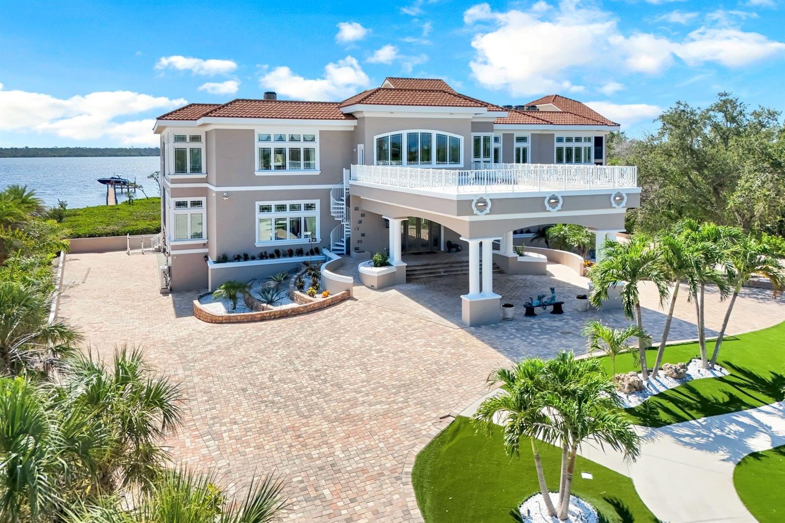 Set on nearly 3 private acres along Lemon Bay, this gated Mediterranean-inspired estate spans 12,789 sq. ft. of resort-style living with unmatched amenities on Florida’s Gulf Coast, all within this private estate. Enter through grand gates and follow a sweeping driveway framed by mature oaks, tranquil ponds, waterfalls, and curated sculptures. The grounds include manicured lawns, a putting green, bocce and volleyball courts, and expansive outdoor recreation. A dramatic porte cochère introduces a soaring two-story foyer with double glass doors, stained-glass transoms, and a glass elevator. Interiors showcase coffered and tray ceilings, stately columns, marble and travertine floors, extensive millwork, and eight fireplaces. The home offers six ensuite bedrooms, 9.5 total baths (primary bath has 3 bathroom sections but counted as 1 in the total), a library with wet bar, a media/family room with projector, fitness and meditation rooms, and rooftop terraces designed for sunset and Gulf views. The chef’s kitchen features dual islands, Sub-Zero and Wolf appliances, wine fridge, ice maker, and walk-in pantry, flowing seamlessly into both formal and casual dining areas. The primary suite includes bay views from a private screened terrace, fireplace, sitting area, spa-like bath, and custom closets, while guest suites offer private balconies, walk-in closets, and baths. Outdoor living is highlighted by a 30×50 resurfaced saltwater pool and spa, full outdoor kitchen, shaded terraces, pool bath, and recreation courts. The property extends to a private dock with boat lift and deeded Gulf beach access. A tiled garage provides capacity for up to 30 vehicles, complete with 10 mini-split A/C systems and extensive storage, ideal for collectors or large-scale entertaining.