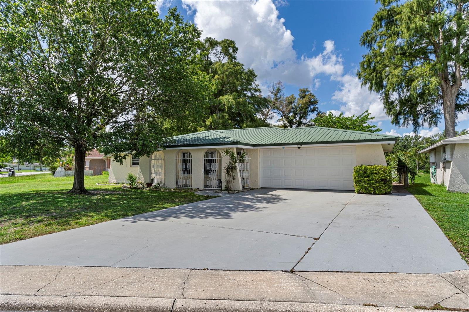 Welcome to your Florida retreat, perfect for snowbirds, first-time buyers, or anyone seeking a home under $300,000! A charming front porch invites you to relax and enjoy the breeze before stepping inside to a bright, open living and dining space with views into the back flex space with views out the back. The spacious primary suite features an zero entry shower bath and garage access, while two additional bedrooms and an updated guest bath are set privately on the opposite side. At the heart of the home, the kitchen shines with a beautiful skylight, 2025 Refrigerator, 2025 Microwave, Range 2020, Closet pantry, reverse osmosis system, and pass-through window to the flex room. Step out to a spacious Florida Room overlooking a private backyard with banana tree, orchid trees, garden area, and no rear neighbors. Outdoor living continues with a fenced side patio adorned with fruiting grapevines. 2008 Metal roof. Extras include a tankless water heater, washer/dryer in garage, and a huge driveway for up to six vehicles—all just minutes from Historic Downtown New Port Richey's activity area with dining and entertainment, and Hudson Beach. Move-in ready and waiting for you!