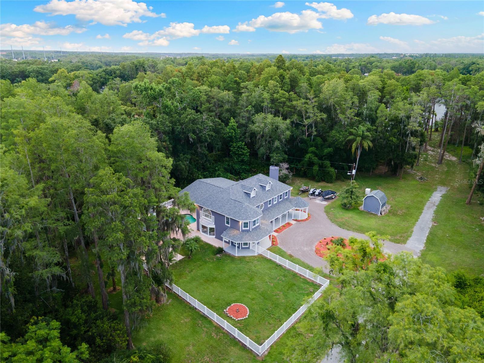 Welcome to 3663 Berger Rd in Lutz, FL – a hidden lakeside gem nestled on 2.36 private acres with direct access to Saddleback Lake, located in the highly sought-after Crenshaw Lakes neighborhood with no HOA or CDD. This beautifully updated 4-bedroom, 3.5 bath estate, offers 4,071 square feet of living space in a serene, tree-lined setting. Designed in a rare Contemporary Victorian style, this two-story residence exudes charm and character from the moment you arrive—complete with a wraparound front porch, second-story balcony off the primary suite, and a peaceful drive down a tucked-away road that feels like your own private retreat. Inside, you’ll find porcelain tile flooring, crown molding, soaring ceilings, and oversized windows that flood the home with natural light. The open-concept kitchen is anchored by a large island with onyx countertops and features a sleek, flush-mounted 350-gallon fish tank built right into the wall—an eye-catching feature that adds personality and style. All bathrooms have been fully upgraded with elegant onyx countertops and spa-inspired custom finishes throughout. The primary suite, located upstairs for added privacy, includes a custom walk-in closet, luxurious ensuite bath with a soaking tub and custom shower, and private balcony overlooking the peaceful backyard. A versatile bonus room upstairs offers the ideal space for a home office, gym, or playroom. Three additional bedrooms are located on the main level, along with a well-appointed laundry room for added convenience. Step outside to your own private oasis, featuring a spacious pool and patio area, along with a covered gazebo complete with a half bath and built-in bar—perfect for effortless entertaining. Follow the serene backyard path down to Saddleback Lake, where you can enjoy jet skiing, fishing, or simply relax and take in the peaceful water views. Additional highlights include a 3-car attached garage with epoxy flooring, a gated, private lot, and zoning for top-rated schools: Schwarzkopf Elementary, Martinez Middle, and Steinbrenner High School. All this, just minutes from shopping, dining, and major highways—offering the ideal balance of seclusion and convenience. Recent updates reflect the thoughtful care and investment poured into this home, including a new roof (2022), three newer AC units (2020), tankless water heater, and Culligan whole-home water filtration system. In 2020, the home also received porcelain tile flooring throughout, California Closet system in the primary suite, and fresh interior paint. More recent enhancements include a new energy-efficient pool pump (2024) and fresh exterior paint (2024). A security system with cameras offers added peace of mind—making this residence as functional and efficient as it is beautiful.
