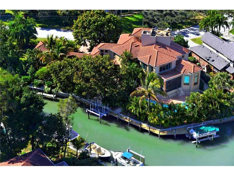 This lovely four bedroom, four and one-half bath home in the secluded community of Paradise Shores, situated on a deep water yacht basin, is just a stone's throw away from Sarasota's open bay. A beautiful family home, with almost 200 ft. of water frontage, sits on an oversized lot with a privately-gated entrance and lush, manicured landscaping. Exquisite features adorn every room. From the impressive spiral staircase in the formal living and private wine cellar, to the summer kitchen and elevated sun deck; you will immediately fall in love with this residence. An ideal space for any gathering, this layout offers a formal dining room just a few steps from the living room with built-in entertainment center, wet bar and soaring ceiling height that stretches up to the second level. A delectable chef's kitchen is equipped with stainless steel appliances, granite countertops, custom cabinetry and a breakfast nook featuring a picturesque Aquarium-glass window. The master suite (and office) is conveniently located on the first level and includes a spa-inspired bath and direct access to the pool deck. Overnight guests will love the privacy the second (or guest) level provides. Complete with three spacious suites, a family room and private access to the sun deck, equipped with a full-summer kitchen and wraparound bar. The crow's nest deck on the upper level is the perfect place to enjoy stunning sunsets and bay views. This home's impressive exterior also features a newer dock and two lifts.