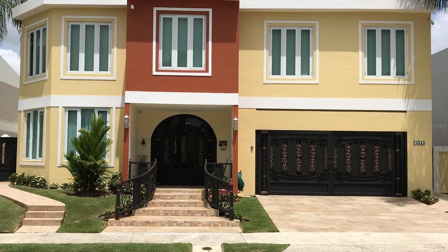 Located in an exclusive, planned, and gated community adjacent to The Montehiedra Outlets and surrounded by supermarkets, shopping centers, restaurants, pharmacy, gas station, banks, fast-food options, Home Depot, and more, this impressive 6,000-square-foot residence redefines luxury and comfort with an impeccable design and thoughtfully curated spaces for maximum enjoyment. It features elegant social areas including a grand foyer, living room, formal dining room, and entertainment lounge; a spacious, fully equipped gourmet kitchen with breakfast area and views of the pool and gardens; five generously sized bedrooms, highlighted by the primary suite with its own foyer, private office, kitchenette, library, two walk-in closets, and a luxurious en-suite bathroom; as well as a guest bedroom with a private bath. Outdoor amenities include a spectacular pool with heated jacuzzi and water recycling system, a covered terrace with wet bar ideal for outdoor entertaining, and an exterior shower. Additional features include a private gym, office, oversized pantry, storage under the stairs, a two-car garage, a 21kW power generator, and security doors—offering privacy, elegance, and an exceptional quality of life.