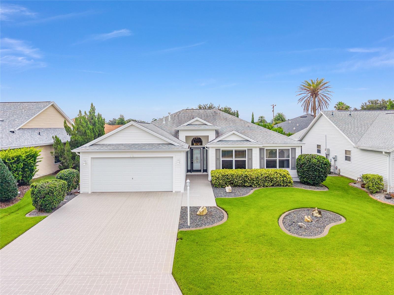 The first time offered for sale since new, this expanded Oleander designer model home with 3 bedrooms (all with closets) and 2 baths, is located in the extremely convenient location of Virginia Trace. Walk or take your golf cart for evening entertainment or to enjoy all the stores, restaurants and offices of Lake Sumter Landing, just steps away from this village and home. As soon as you enter this home, note the expansive, light-filled living room with its volume ceiling and large, beautiful window straight ahead. Be sure to check out the spacious kitchen with plenty of white cabinets, granite countertops, room for a dining table and featuring a tall pantry cabinet, and useful center island with both extra storage and seating. This home has been expanded and now has a spacious dining room or Florida room adjacent to the kitchen area. This expanded room has easy access to the kitchen by a pass-thru window and also features built-in cabinets, Corian counter, and room for a wine refrigerator. Both bathrooms have vessel sinks and stone counters. This one owner home that has been lovingly cared for and is priced to sell. A new water heater was installed in 2018 and A NEW ROOF in 2020. The BOND IS PAID, and a one-year Broward Warranty is included.
Please stop by soon to decide if this home could be your new Villages home!