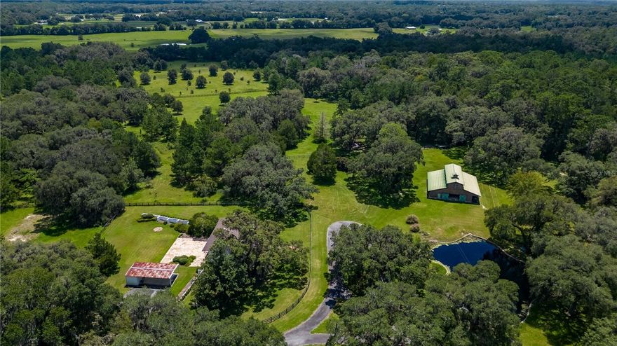 A stunning opportunity to enjoy the best of Florida’s natural beauty for years to come! Comprising 200 acres in NW Marion County’s iconic horse country, this property has a unique quality not often seen on the market– the full property is a Conservation Easement that is considered a Stewardship Forest and certified Tree Farm. In fact, this property is the only Conservation Easement currently offered for sale in the Marion County area. Several species call the property home and flourish amongst the mature trees and park-like setting. Two residences are currently established on property: The main home was renovated in 2000 and features a variety of unique features. The stone accents throughout the exterior and interior portions have been sourced directly from the land, as have the hardwood flooring throughout. Large windows allow for ample natural lighting as well as sweeping views of the surrounding property. No detail has been overlooked in this home, from the top-of-the-line appliances to the open, flowing layout. Uniquely, the home also includes a stunning attached greenhouse that allows for year-round gardening for those with a green thumb. The secondary residence on the property is a lovely 2-storied, 3,800 sq.ft. home with lots of opportunity to update if desired. A large covered front porch with column accents welcomes visitors inside to enjoy the stately appointed interiors. The bottom floor of the home serves as a huge, private in-law suite with full amenities for added convenience to long-term guests. To the back of the home is a large stone patio that overlooks the nearby paddocks and open greenery. A separate carport is located nearby and is equipped with additional storage options. Also established on the property is a stunning center-aisle barn with a total of 5 stalls, feed and tack room, hay storage, and an open upper loft. Four bay doors allow for extensive equipment storage, and fans run throughout to keep the air moving. A picturesque pond is also nearby the barn, with a lovely fountain feature, seating area, and a small dock. Those looking to raise more than horses will love the additional chicken coop with fencing and wire enclosure for added safety. Several trails run throughout the property, offering ample opportunity to explore and enjoy the property’s natural landscape. This stunning farm offers a highly convenient location just 9 minutes from HITS and 25 minutes to WEC, with a variety of equine service providers, retailers, and veterinarian care in the area. Both Gainesville and Ocala’s many shopping, dining, entertainment, and medical opportunities are just a scenic drive away. This farm is a unique opportunity for those who desire a sustainable lifestyle with abundant privacy.