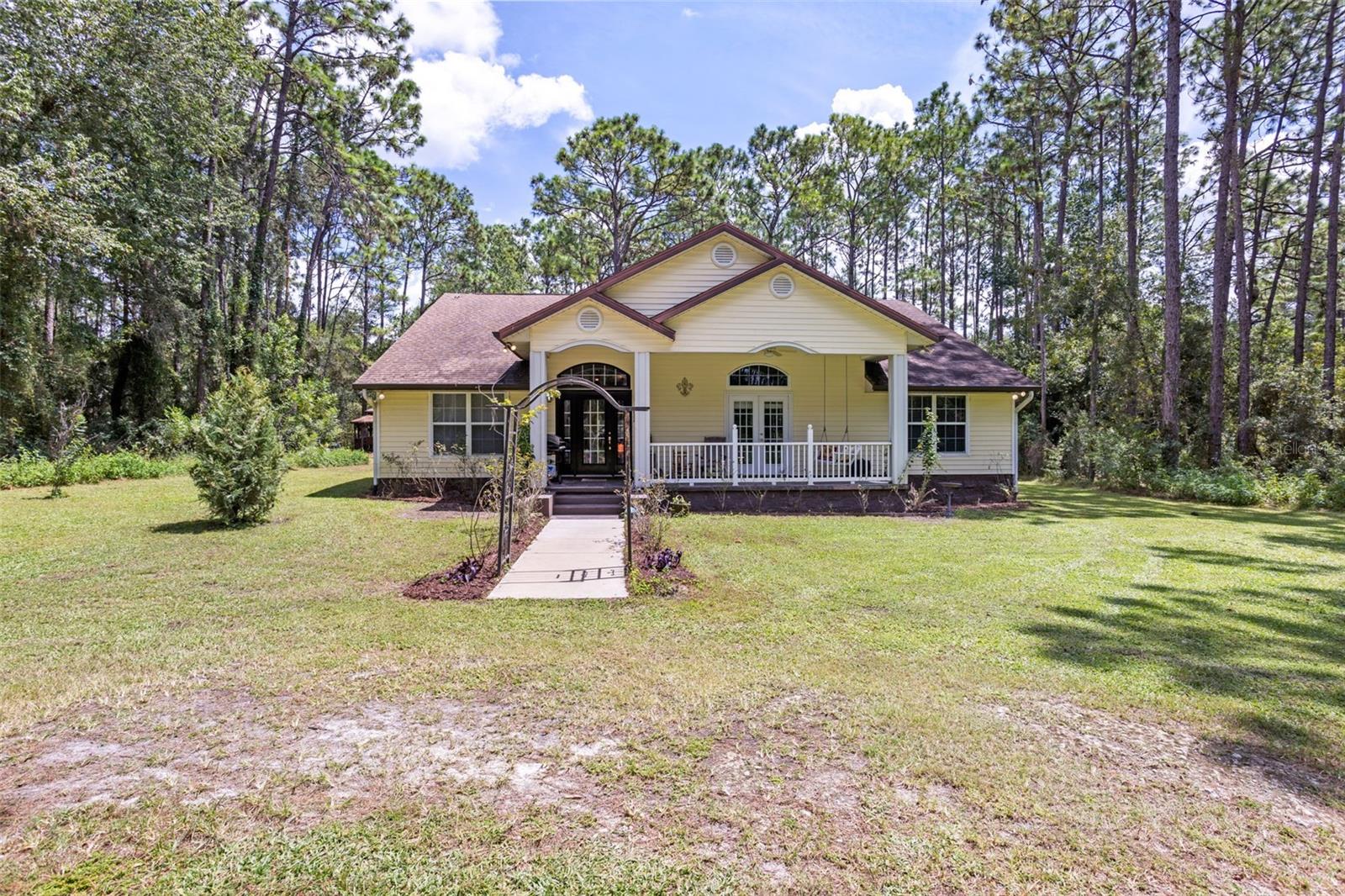 Cue the opening scene: a “cute-as-a-button” 3BR/3BA + office (˜2,640 SF) tucked on 5 wooded acres just minutes from The Villages. Meandering trails lead to a round gazebo with swing and a cozy fire-pit patio, while a wide covered front porch (perfect for rocking chairs or swings) sets the laid-back tone. Inside, a dramatic vaulted great room centers on one of 2 stone wood-burning fireplaces; French doors open to an oversized screened porch for effortless indoor/outdoor living. The kitchen pairs stone countertops with custom cabinetry and abundant storage—bathed in natural light for an inviting, everyday workspace. With broad, uninterrupted counter runs, you’ll stage appetizers, prep main courses, and still have space for dessert—no back-and-forth shuffle. It’s a true host’s hub that handled joyful gatherings here for year; wood floors run through most of the home. A second wood-burning fireplace adds warmth, and the dedicated office flexes as guest space or creative studio. Multiple outbuildings/sheds expand your options—each with electric (several with water & A/C) plus one building with a small kitchenette (ideal workshop/studio/office; not in living SF). Practical perks: 2-car carport, gutters, concrete foundation, wood frame/siding, and—per public sources—no designated flood zone (buyer to verify). Minutes to dining, shopping, nightly entertainment, golf, and healthcare in The Villages; easy access to US-301, I-75 & the Turnpike. loved by performers and the backdrop to joyful gatherings (including 3,000+-egg Easter hunts!), this private retreat was made for entertaining—come see your next act and schedule a private showing today.