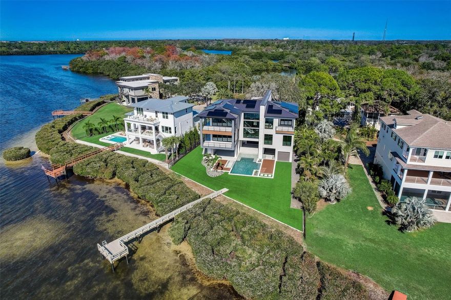 BRAND NEW TO TAMPA BAY! A masterful achievement of concept and design. DAZZLING CONTEMPORARY DESIGN ELEMENTS AND CLEAN, MINIMALIST ARCHITECTURAL CONCEPTS, BRING TO LIFE THIS ASTONISHING COASTAL LUXURY WATERFRONT MASTERPIECE! A majestic curbside presence, a towering 28ft-high Porte cochere and a prodigious 40ft-high foyer, introduce a home with rare presence and grace. gleaming lightwork, tall, brilliantly finished ceilings, lavish materials, precision workmanship and spectacular sweeping views of the waterfront deliver an unforgettable living experience. With attention to perfect lines and the smallest of design details, every day will feel new, exciting and different. This home’s splendor and beauty are engineered with a remarkable level of quality through simplicity and symmetry. With Full Block Construction, 18kw Solar Panels, Ryan Hughes Custom Designed Pebble Tec Salt Water swimming Pool.  The trappings of a sumptuous gourmet cooking experience lay hidden behind the walls of a custom-built kitchen with high-end Wolf and Subzero appliances, gas cooking, and waterfall countertop – all supporting a beautiful island prep-center bar with pearl white quartz surfaces, and a fine butler’s pantry. The impressive waterfront great room is balanced by a terrific waterfront dining area, the uncluttered allure of the  executive office, and an exceptional luxury guest bath. With grand views of the waterfront, private balcony access and two large walk-in closet systems, the owner’s suite on the 3rd floor is inspiring, tasteful and inviting. The owner’s bath is a lavish, pampering retreat – with elegant vanities, superb 48x48 flooring, Brizo and Toto fixtures and multi-head rainshower. Also Upstairs, discover 2 bedroom suites with private balconies and commanding views of the waterfront. All bedrooms are oversized, provide custom closet systems, have direct water views and are en suite, with plush full luxury baths. Step outside to a waterfront oasis with three distinct sitting areas – all brought together by rich landscaping & fabulous views. Your waterfront features include new turf, large composite dock, kayak/paddleboard launch, and moorings for your 2 story pontoon or deck boat! Stunning pool/spa. 3-stop commercial elevator and much more! Best waterfront commuting location in Tampa Bay. Close to the Courtney Campbell Bridge, reach the beach in 10 min, downtown Clearwater in 10 min and Tampa Airport in 25 min.