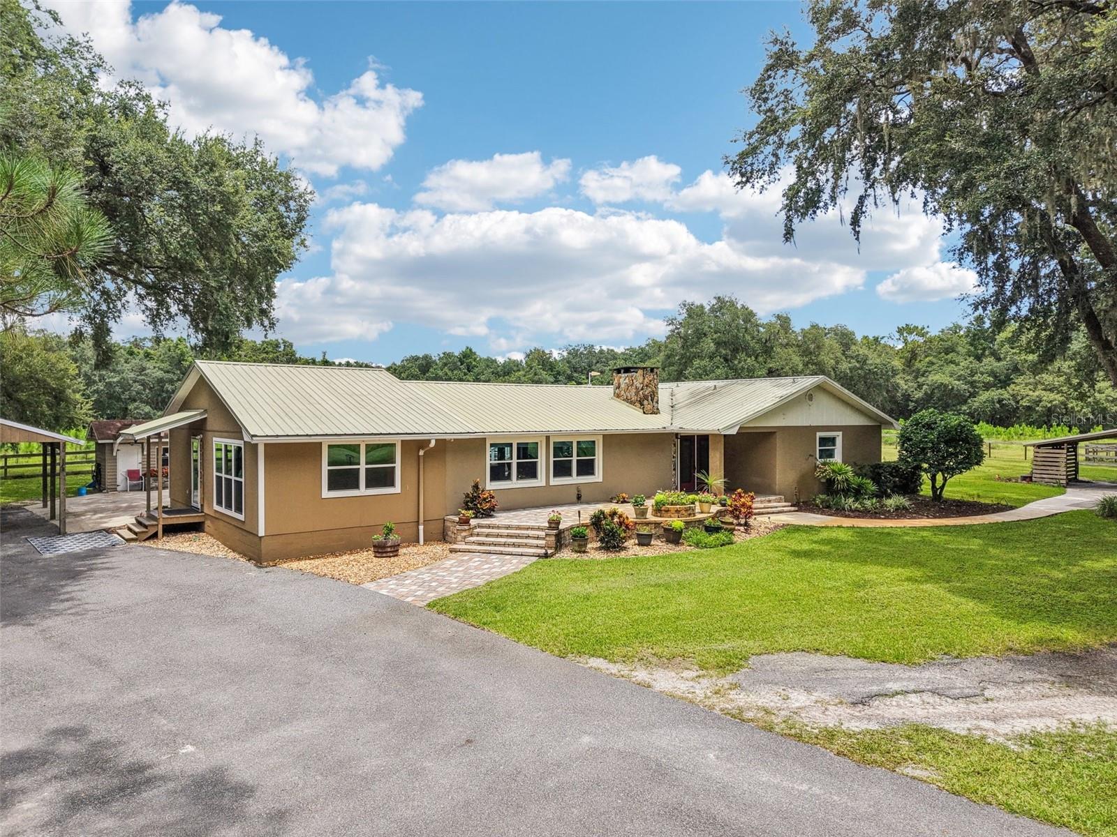 Sustainable. Stylish. Self-sufficient. Welcome to 5117 County Road 316A in Bushnell—a rare 16.8-acre estate that balances self-reliance with Southern hospitality, functionality with finesse. Behind a private electric gate and paved driveway shaded by mature oaks, this hidden gem unfolds into a private, park-like setting rich with both comfort and capability.
The main 3-bedroom, 2-bath home features upgraded hurricane-rated windows, a 2020 HVAC system, 30 high-efficiency solar panels, and a matching metal roof and gutter system. Inside, the warm galley-style kitchen offers stainless appliances and a 2020 gas range. The living room is anchored by a large natural Florida limestone fireplace that mirrors the custom glass front entry—a striking architectural detail. Recent additions include a light-filled sunroom and a walk-in pantry that would make any homesteader swoon.
On-site accommodations continue with two separate guest or rental-ready living quarters: a spacious 2-bedroom (approximately 540 sqft), 1-bath apartment on the ground floor with granite counters and open-concept design, and an upper-level 1-bedroom, 1-bath apartment (110 sqft)with its own entrance—each equipped with laundry and private access.
Recreation and relaxation are everywhere you turn. There are two pickleball courts, a full frisbee golf course that winds through approximately 4,000 planted pines, and an above-ground pool with composite decking and adjacent full bathroom. A paved entertainment courtyard with custom lighting, covered grilling area, and lush upgraded landscaping create an ideal backdrop for hosting. The grounds are fully fenced and meticulously maintained.
The estate also boasts serious infrastructure: a 24×40 enclosed pole barn with HVAC, hot water, two roll-up doors, shelving, and 20-amp outlets every 10 feet; a dedicated climate-controlled shed for the solar battery system; a 3-bay concrete equipment barn; an RV pad with 50-amp service and water; a 20kw Generac whole-house generator; a 500-gallon gas tank with pump; and underground electric.
A chicken coop with feed room and an orchard of peach, orange, plum, pear, persimmon, and loquat trees add the perfect touch of rural self-sufficiency. The approximately 4,000 planted pines offer not only shade and fresh air but also agricultural tax savings and the potential for future income when harvested.
Located just minutes to I-75, under an hour to Tampa or Orlando, and convenient to The Villages, shopping, dining, and services—yet worlds apart in peace, privacy, and possibility.
Open and available 7 days a week for private viewing. Very easy to show but by appointment only. Proof of funds required for appointment. Call today.
It’s the kind of place where you can host a wedding on Saturday, harvest your orchard on Sunday, and still make it to Tampa by Monday. Built in 1979, but beautifully maintained and thoughtfully upgraded over time, this estate is prepped for whatever the future holds—be it family, income, or independence.