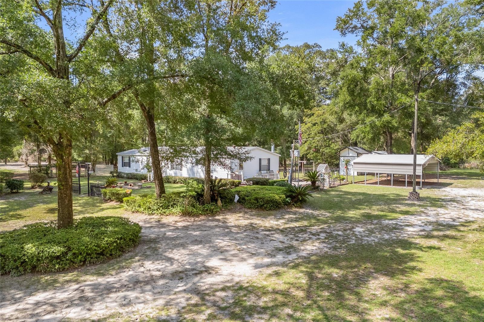 Nearly 7 acres of privacy and serenity surround this charming 3-bedroom, 2-bathroom home! Tucked away in Gilchrist County with a High Springs address, this property offers the best of both worlds—peaceful country living with quick access to local attractions and everyday conveniences. Just 2 miles from Poe, Blue, and Ginnie Springs, you’ll have Florida’s most beautiful natural treasures practically in your backyard. From the moment you walk in, you’ll feel the warm, inviting atmosphere that makes this house feel like home. The interior features two spacious living rooms, including one with a cozy fireplace, a formal dining room, and a bright eat-in kitchen with a window overlooking the property. The primary suite is a true retreat, complete with separate his-and-hers vanities, and a large garden tub for relaxing after a long day. All bedrooms include walk-in closets, providing ample storage throughout. Step outside and enjoy the peaceful setting from the side deck, perfect for entertaining or simply soaking in the quiet surroundings. Additional highlights include a carport, two storage sheds (one with a loft), and a 3-zone irrigation system. With mature trees, abundant wildlife, and plenty of room for animals, the possibilities here are endless. Best of all, there’s no HOA or deed restrictions—so bring your garden, your toys, and your dreams. This property truly has space for it all. Located just minutes from downtown High Springs with its charming shops and restaurants, and only a short drive to Gainesville and Lake City, convenience meets tranquility in the perfect balance.