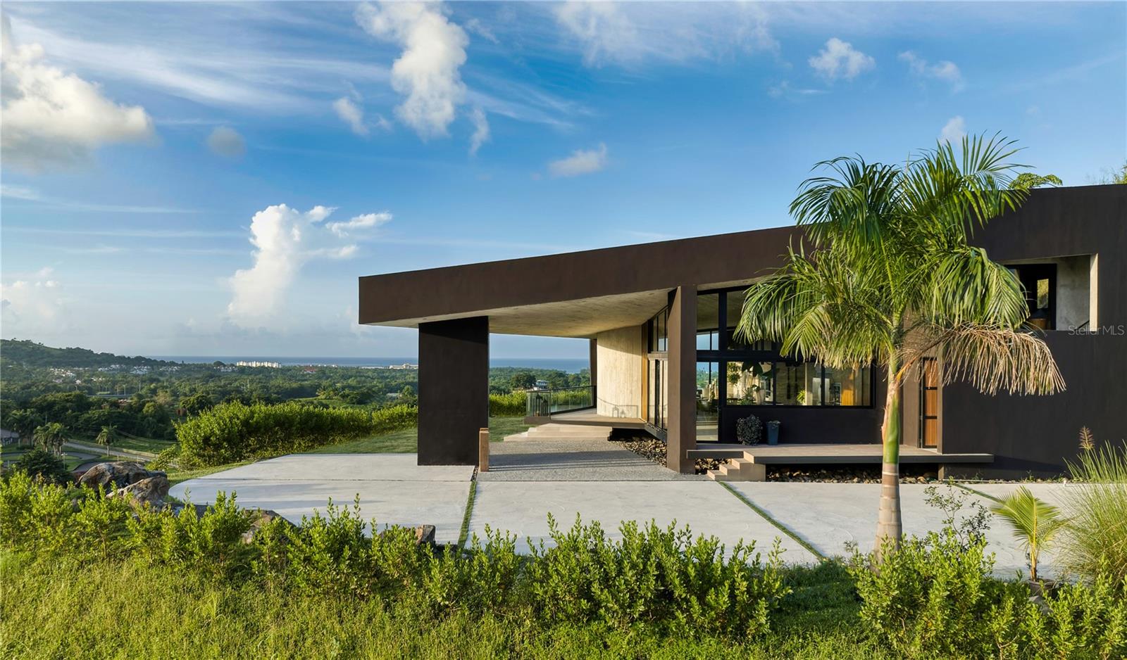 This modern architectural marvel is impressively positioned within the mountains of Luquillo in the heart of the El Yunque Rainforest, showcasing mesmerizing ocean and mountain views. Designed to perfection and every comfort realized, Hacienda Les Chevaux is located in the exclusive neighborhood of estate homes next to the well known Hacienda Carabali Ranch. This extraordinary home offers a rare and one of a kind Equestrian lifestyle within the backdrop and proximity to Rio Mar Resort.
The residence's well-appointed interior layout spans approx. 3,823 Sq. Ft. and the covered outdoor area provides approx. 455 Sq. Ft. of additional space, for a total of 4,278 sq. ft of shere perfection.. The property's first level features floor to ceiling glass walls with a height of 13’5’’ overlooking a waterfall cascading from the hilltops above, as well as a living room, dining room, designer kitchen, two ensuite bedrooms, including the primary suite with direct access to the terrace with pool, outdoor kitchen with BBQ area and powder room.
The second floor with separate private entrance includes a third ensuite bedroom, perfect for hosting family and friends. The lower level serves as a guest suite or additional entertainment space, along with your own private gym.
Luquillo, also known as the “Capital del Sol” or the capital of the sun, is renowned for its breathtaking beaches such as Playa Azul and Playa Fortuna. . Enjoy the epitome of island living in the mountains, affording unparalleled privacy and tranquility while still being in close proximity to San Juan. A distinctive highlight for the new owner of this property is its inclusion of a membership to the prestigious Rio Mar Country Club, enhancing the owner's lifestyle with access to world-class amenities and recreational opportunities.