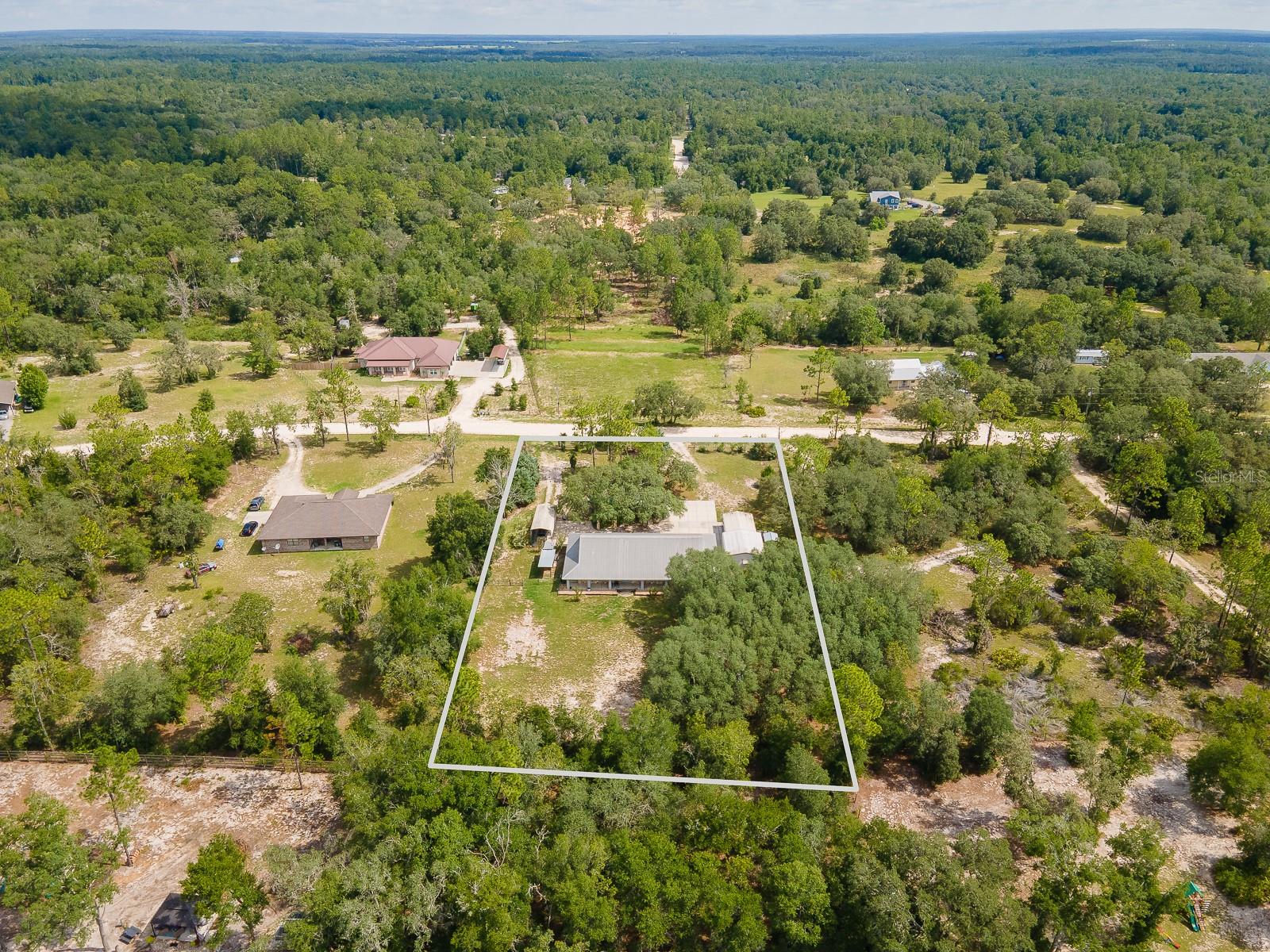 This spacious 4-bedroom, 3-bathroom stone home sits on a generous 1.24-acre lot and features an open-concept layout with a split floor plan, offering both comfort and privacy. Perfectly positioned just over the county line in Levy County, it allows you to enjoy the benefits of lower property taxes while remaining conveniently close to shopping, schools, and medical facilities. The fully fenced property offers two wide double-gate entries and a variety of outdoor amenities: two free-standing carports (12x30x12 and 17x26), a large 20x22 workshop, a 12x24 shed with room A/C, and a 16x16 tiki bar complete with an outdoor kitchen featuring a gas grill, pizza oven, sink, and a private bath house. A full wraparound porch frames the home, adding charm and space for relaxation or entertaining. Offering the best of country living with practical features and easy access to city conveniences, this unique property is truly one-of-a-kind.