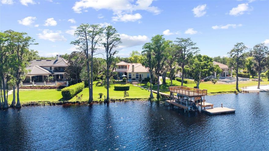 Tucked away within the gated community of Northbridge at Lake Pretty, this exceptional lakefront estate is one of only six homes situated directly on exclusive Lake Pretty—a pristine 100-acre ski lake in the heart of Odessa. Offering over 4,300 square feet, this 4-bedroom, 4.5-bathroom residence also features a dedicated office and expansive bonus/theater room, with every bedroom enjoying its own private ensuite. From the moment you enter, you’re welcomed by abundant natural light and a stunning formal living space highlighted by a large bay window that perfectly frames the home’s most captivating feature—the breathtaking lake views. Just off the formal living area, the private right wing of the home includes a dedicated office, powder room, and an expansive primary suite retreat. The primary bedroom features double tray ceilings with crown molding, French doors leading to the outdoor patio, and two custom walk-in closets with built-ins. The en-suite bathroom is thoughtfully designed with dual vanities, a large enclosed shower, and a relaxing jetted tub. The kitchen serves as the centerpiece of the home, beautifully appointed with high-end granite countertops, two-toned cabinetry, and a large center island with farmhouse sink. Premium appliances include a Viking refrigerator, Viking 6-burner gas range, Bosch dishwasher, built-in GE double ovens and microwave, along with a hidden pull-out coffee bar for added functionality. A butler’s pantry passthrough with a wine refrigerator and additional storage elevates both convenience and entertaining. The kitchen seamlessly flows into the family room and dining nook, where oversized windows flood the space with natural light and showcase serene water views. A private wing off the main living area includes two bedrooms and a versatile bonus room, currently designed as a theater but easily adaptable as a game room, fitness space, or golf simulator. Bedroom two features a spacious ensuite with a separate makeup vanity and large walk-in closet, while bedroom three offers beautiful lake views and an ensuite bath that also functions as a pool bath. Upstairs, a private retreat awaits with an additional bedroom featuring its own ensuite, walk-in closet, and double doors leading to a balcony overlooking the pool and expansive lake views—an ideal space for guests or multigenerational living. Designed for true indoor-outdoor living, the backyard is a showstopper. Enjoy a covered lanai with a fully equipped outdoor kitchen including a grill, vent hood, mini refrigerator, ice maker, and bar seating. The saltwater pool and spa with spillover feature create a resort-style setting, while paver pathways lead down to a custom lakeside fire pit nestled among mature cypress trees. The private two-story dock is built for both recreation and entertaining, complete with a boat lift accommodating up to 10,000 pounds, dual jet ski lifts, and an upper-level deck offering panoramic views of the entire lake. This is a rare opportunity to own one of the most coveted lakefront properties in Odessa, combining luxury, privacy, and true waterfront living.