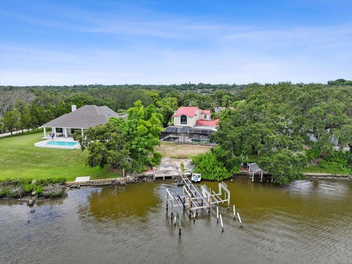 A hidden diamond in the rough! Rare opportunity to own a 1.65-acre waterfront estate in charming Safety Harbor, Florida. Tucked away at the end of a gated drive, this expansive two-story, 5-bedroom, 3.5-bath pool home sits on prized Old Tampa Bay frontage— offering stunning sunrise views and a tranquil waterfront lifestyle. With over 4,000 square feet of living space, the home showcases rich architectural elements including marble floors, soaring ceilings, ornate columns, a dramatic oak staircase with wrought iron accents and a Juliet balcony. Sliders across the back of the home and striking arch-top windows fill the interior with natural light and frame sweeping water views. This home is being sold AS IS, and the price reflects needed updates—presenting a rare chance to renovate or rebuild in one of Safety Harbor’s most coveted locations. Just over a mile to Philippe Park’s public boat ramp and minutes from charming downtown Safety Harbor, known for its marina, shops, dining, festivals, and waterfront parks. Enjoy quick access to major roads, Tampa International and St. Pete/Clearwater airports, Honeymoon Island (10 miles), Clearwater Beach (13.6 miles), and downtown Tampa (19 miles). A truly unique opportunity to create your waterfront dream estate. The flexible layout includes a spacious living room with a wood-burning fireplace and French doors to the family room and kitchen. The kitchen features stainless steel appliances, a breakfast bar, and overlooks the family room and adjacent dining/sunroom with a wall of glass doors. One of the three downstairs bedrooms is a second primary suite with French doors to the sunroom and features an ensuite bath with a spacious vanity and tub/shower combo. Upstairs, a grand entry framed by pillars leads to the primary bedroom featuring hardwood floors, soaring ceilings, a private Juliet balcony, and sunrise views. The primary bath includes dual vanities, a soaking tub, tile floors, and a large walk-in shower. The fifth bedroom is also upstairs and is an ideal flex space—perfect as an office, den, or media room. Step out of one of the many glass sliders to a pool and patio area ideal for relaxing or entertaining. Complete with a screen-enclosed pool, covered seating area, koi pond, and tranquil waterfall, this outdoor retreat is all set against the serene backdrop of Old Tampa Bay. Car enthusiasts and hobbyists will love the massive five-car detached garage with four garage doors for drive-through access, plus a separate RV garage/workshop. Additional highlights include a huge 12x16 utility/laundry room, no HOA or deed restrictions, and No Flood Insurance required (Flood Zone X). Although no water entered the home during recent storms, the dock with two boat lifts will need to be rebuilt. Interior photos and tours available to serious buyers only. Don’t miss this incredible opportunity. Call today for additional information.