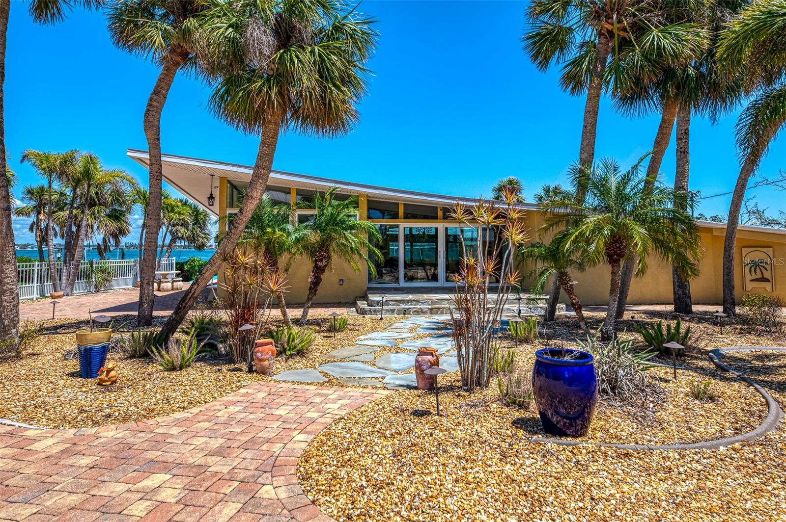 This is more than just a home—it’s a rare opportunity to own a unique, waterfront lifestyle on Manasota Key, where architectural elegance meets the tranquility of Lemon Bay. Discover a rare blend of iconic design and coastal elegance in this stunning Frank Lloyd Wright-inspired home, perfectly positioned on nearly half an acre along the tranquil shores of Lemon Bay. Located on Manasota Key, this FURNISHED, 2-bedroom, 2-bathroom residence has been thoughtfully remodeled after recent hurricanes, seamlessly merging mid-century architectural charm with today’s modern comforts. With the addition of a spacious 720-square-foot studio apartment above the garage, this property offers the flexibility to function as a private family compound, ideal for multigenerational living or hosting guests in style. Enjoy peace of mind with impact-rated windows and sliders throughout the home, and savor the chef’s kitchen featuring solid wood cabinetry, granite countertops, and all-new stainless steel appliances. Step outside to your expansive enclosed lanai, the ultimate outdoor oasis with a heated saltwater pool—perfect for entertaining, relaxing, or soaking in the serene waterfront views. For boating enthusiasts, the property includes a deeded 16,000- pound boat lift (added in 2018) and dock. There is also access to a shared community dock (first come, first served), used by only four owners—ideal for additional watercraft. Deeded beach access on the property means your toes can be in the sand in just minutes. The home also features a sprawling 5-car garage (fits up to 7 vehicles) with ample room for storage or a workshop, plus a dedicated area for RV parking. Above the garage is a fully furnished studio apartment, newly built in 2023, with luxury vinyl plank flooring, granite countertops, and stainless steel appliances. Thoughtfully designed, this space is also plumbed for a future elevator, providing long-term flexibility and accessibility.—making it perfect for guests, rental income, or multigenerational living. Additional features include a 10x20-foot storage shed, a sprinkler system (with some zones needing repair), and lush landscaping that enhances the natural beauty of this unique property.
