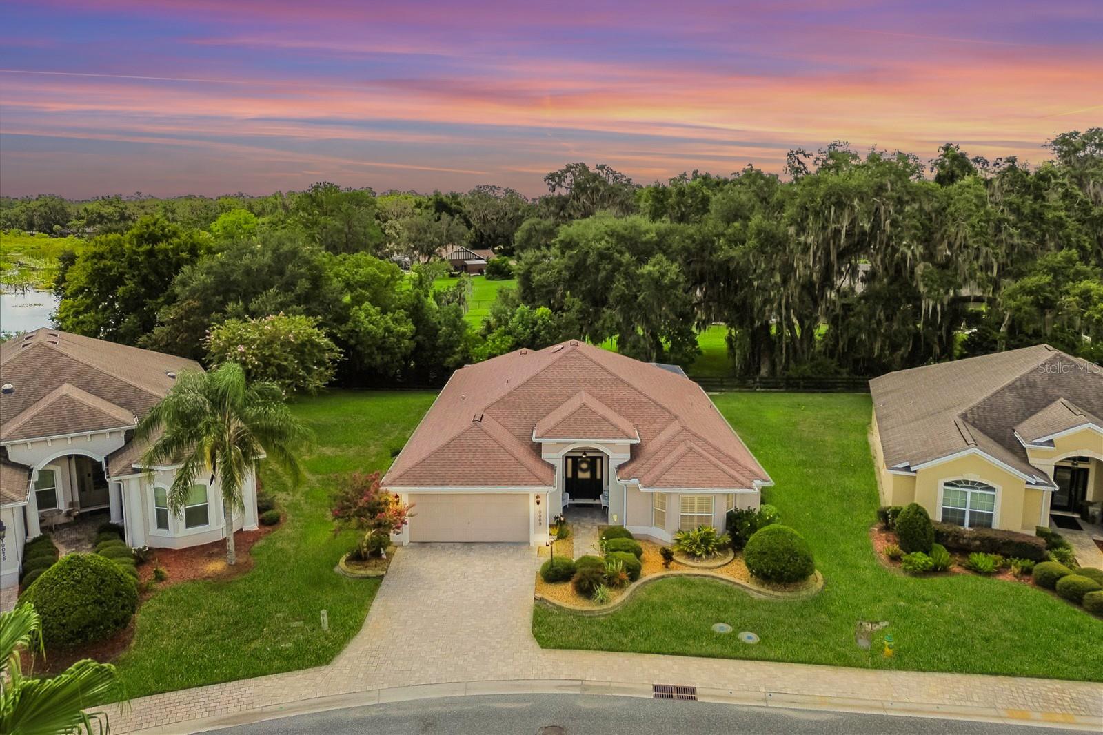 This beautiful home offers a rare combination of privacy, space, and resort-style living. Nestled on a pie-shaped homesite backing to a charming 4-board fence, there’s ample room for a future pool — and with a sneak-a-peek of Lake Miona, the view would be even more impressive with a pool or birdcage addition. The exterior features brick paver walkways, stacked stone accents, and low-maintenance landscaping with rock-filled flowerbeds. Inside, you’ll find large ceramic tile in the wet areas and wood laminate flooring throughout the rest of the home — no carpet — and plantation shutters on all windows.
The kitchen is a showstopper, boasting white cabinetry, stainless steel appliances (including a glass-top range), granite countertops, tile backsplash, under-cabinet lighting, and stylish pendant lights. The primary suite offers a tray ceiling and a spa-like bath with dual vanities and a walk-in shower. Pocket sliders lead to an oversized lanai with brick paver flooring and an added birdcage, perfect for soaking up the Florida sun. The extended 2-car garage — an extra 4 feet forward — provides plenty of space for vehicles, golf carts, and more. Located in Lakeside Landings, a sought-after gated community just minutes from The Villages and Lake Miona, residents enjoy an impressive array of amenities: a 13,000+ sq. ft. clubhouse, resort-style pool and spa, fitness center, pickleball and tennis courts, bocce ball, putting green, and a private beach with dock access to Lake Miona. There’s also a dog park, walking trails, and an active social calendar, making it easy to enjoy the Florida lifestyle to the fullest.