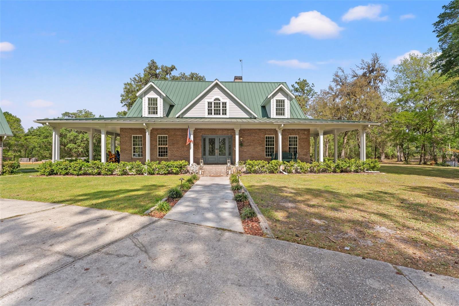 Welcome to 105 acres of pure Florida paradise—where rolling hills, open pastures, flowering fields, and towering grandfather oaks create a breathtaking backdrop for a truly exceptional ranch lifestyle. This versatile property is a harmonious blend of beauty, function, and income potential, featuring a mix of planted pines for future return, miles of cut riding trails, and stunning views at every turn. At the heart of the property sits a beautifully remodeled 4-bedroom, 4-bathroom brick home offering over 4,600 sq ft of refined living space. With a wraparound porch that welcomes you with classic country charm, the interior is a seamless mix of modern luxury and cozy warmth. The bright, open floor plan flows effortlessly through expansive common areas—ideal for large families, entertaining, or holiday gatherings. Three of the four bedrooms are private en-suites, providing space and comfort for guests or multi-generational living. Above the oversized garage, a spacious 1,200 sq ft guest quarters includes a full bathroom and full laundry room—perfect for a media room, game room, or secondary living space. But it's the equestrian and agricultural amenities that set this property apart. The main barn is a dream: 13 oversized European-style stalls (eight of which are 12x24), two wash bays, a feed room, tack room, and a VIP lounge complete with kitchen and gathering space. With 17 rotational pastures and brand new fencing—including 12 pastures with 10-foot boundary runs—this setup is ideal for stallions, breeding, or any serious horse operation. The animal accommodations continue with eight run-in stalls, a covered 80-ft round pen, and four additional outbuildings currently used for small livestock, hatcheries, and greenhouse gardening. A secondary center aisle barn with 12 additional stalls and a 200x300 outdoor arena is under construction and will be fully operational by the end of May. Need a place to unwind? Head to the property's private 5-acre lake—stocked for fishing and surrounded by stately pines, complete with a dock, picnic area, and total tranquility. This is more than a ranch—it's a legacy estate for those who want to live, work, and breathe the country lifestyle in style.