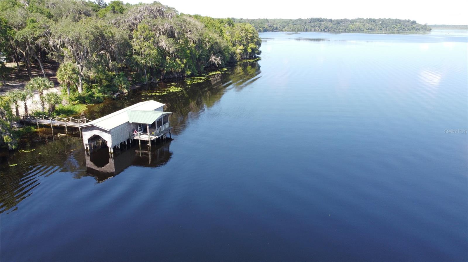 This 4 acre property overlooks Rodman Reservoir and the Ocklawaha River. The large 3 bedroom, 2 1/2 bath home has an attached 1/1 in-law suite, a screen enclosed pool and a 30x60 detached garage. Features include a beautiful stone fireplace with a cypress mantel in the living room, a separate office/family room, abundant kitchen cabinets and counter space, inside utility room, vinyl plank flooring and tile throughout, updated HVAC units, primary suite with a walk-in closet plus double vanities and a step-in corner shower. The 1/1 in-law suite has its own kitchen and a private entrance in addition to being accessible from the main home - Great layout for extended family or potential rental income. Large 12x41 glass enclosed porch overlooks the pool area. Boathouse and dock for your enjoyment. The boathouse offers 2 boat slips, a screened porch and incredible views. FL Greenway area is located between the property line and waterfront. Situated on a paved road in the Ocala National Forest between Fort McCoy and Salt Springs.