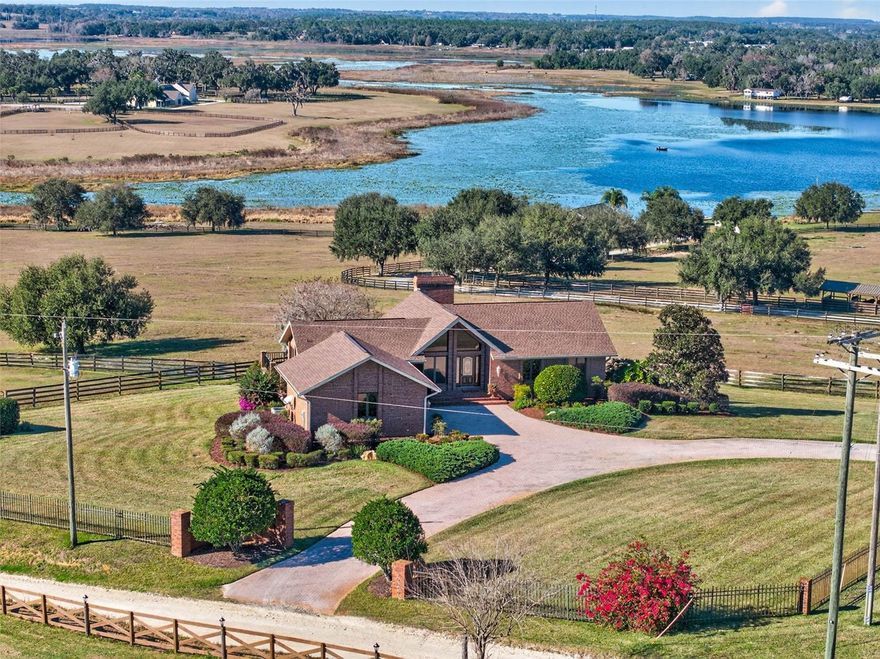 Welcome to an extraordinary hilltop estate in Dade City on nearly 33 acres of fenced, private land with sweeping views of Lake Pasadena and an impeccably detailed primary residence. The property encompasses fenced pasture and rolling land providing endless possibilities for agricultural enthusiasts to have horses, chickens, cows, sheep, goats and other farm animals, or who want to indulge in gardening, farming, boating, fishing or large-scale entertaining. The lake views and hilltop privacy create a serene timeless setting. The brick-clad home crowns the property, offering elevated panoramas and a striking curb presence. Enter the home on the main level the primary suite is a serene retreat with crown molding, a spa-like bathroom featuring a garden tub and separate walk-in shower, while a second bedroom currently used as an office and an adjacent guest bath complete the main level. The newly remodeled kitchen offers rich wood cabinetry trimmed in crown molding, beautiful granite countertops, a large island with cooktop, pull-out cabinets and drawers, and stainless KitchenAid appliances, plus a separate wine/beverage dry bar ideal for entertaining. The upstairs family room is warmed by a wood-burning fireplace, exposed wood beams, and expansive windows framing the property and lake beyond. The lower level expands living and entertaining options with a large great room anchored by a second brick fireplace, a huge bonus room, guest bath, and sliders that open directly to the grounds. Two generous downstairs bedrooms include a secondary owners’ retreat or mother-in-law suite with a private, spa-like bath and Jack-and-Jill configuration, bringing the primary house to four true bedrooms and four full bathrooms. Down the hill near the lake is a second home with 2 bedrooms perfect for extended family, guests, staff, or rental income. Dade city is a quaint town with a historic downtown featuring Old-Florida charm. The home is a few minutes off I-75 which has easy access to Wesley Chapel's shopping, restaurants, bars, Hospitals etc. Call today to view this spectacular property!