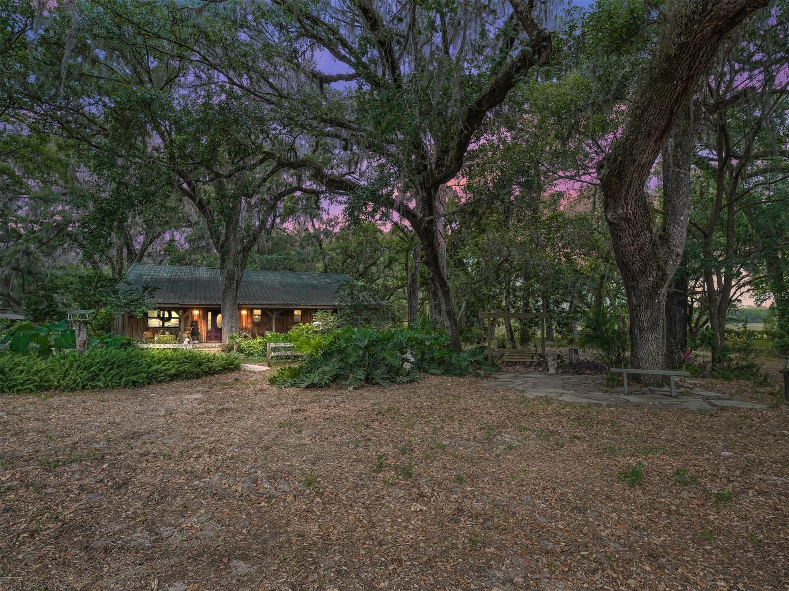 Privacy abounds at this 15 acre horse property centrally located in Bushnell at the end of a dead-end street - no roads touch this property! Enter the property though the automated gated entryway complete with zombie lock for added security. Pass several cross fenced paddocks and the drive leads to the home nestled in a mature hammock of age old oaks and a variety of stunning mature landscaping, which you will find throughout the property. The large and welcoming covered front porch is sure to be one of your new favorite places, perhaps until you find yourself rocking on the covered back porch. Inside, this special home features hardwood & tile flooring and vaulted wood ceiling with a spacious and functional open layout, perfect for entertaining. The open kitchen overlooks the living space and offers a long island with room for several barstools, soft-close cabinetry, a closet pantry and Jenn Air dual fuel range with gas cooktop and double electric ovens. The primary suite features access to the back porch and an ensuite bathroom with walk-in shower. The split bedroom layout offers two additional bedrooms on the opposite side of the home with a shared bathroom in between. There is also a laundry room leading to the front porch, doubling as a mud room. You are sure to appreciate the two thoughtfully designed, center aisle horse barns with 13 stalls measuring 11' x 14'. The "Stud Barn" has 4 reinforced stud stalls, 2 regular stalls and an attached 1,300 square foot shop/equipment storage area with industrial shelving and doors on 4 sides. The "Mare's Barn" has 7 stalls, a cedar walled tack room with tree log saddle racks and a separate lab room. You will also find inspection chutes and cross tie areas at both barns, wash rack, 1/10 mile riding arena, 7 cross fenced Pensacola Bahia pastures with water to each, 4 paddocks, private pond, greenhouse, 3 duck/chicken pens, and an incredible array of plants and wildlife. This exceptional property, comprised of two parcels (10 and 5 acres each) with separate power access, also offers an ideal layout for a multi-generational family compound or private homestead—with ample space to add guest homes, additional dwellings, or extended living quarters as desired. Centrally located just 3 miles to the soon-to-be Aldi shopping center and approx. 1 hour from Tampa, Orlando or Ocala with easy access to i75 and the FL Turnpike. This is truly a property you must experience in person to appreciate all it has to offer. Please enjoy the attached video and 3D tours!