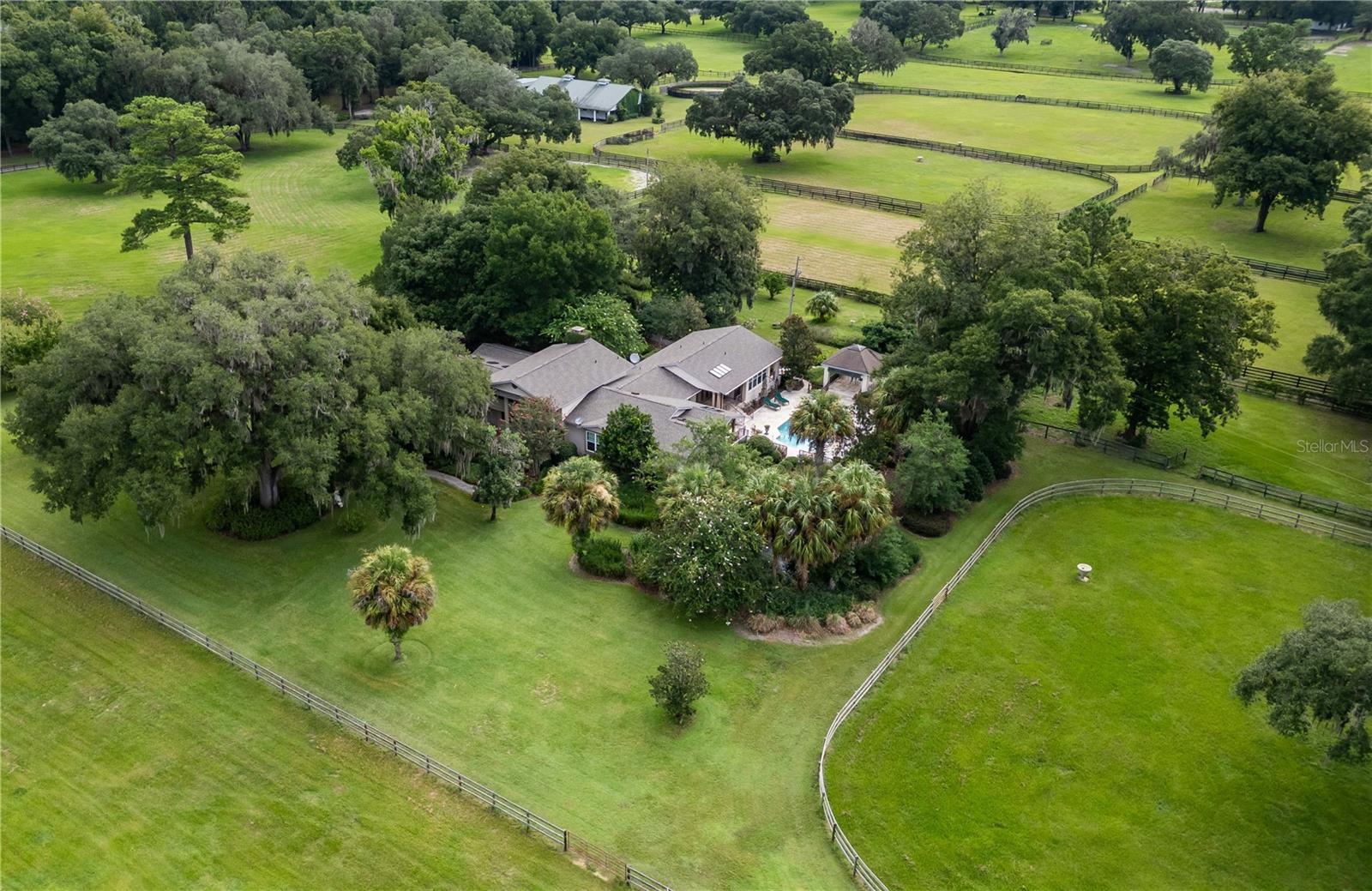 Located on a quiet country road in NW Marion County, River Mist Farm offers 42 acres of spacious pastures, glorious live oaks, and spectacular gardens and privacy. As a private horse facility the farm has been the birthplace of multiple stakes winners and champions and
offers stunning landscape for whatever equestrian discipline you pursue. A beautiful canopy of crepe myrtles shade the driveway as it leads towards the 3-bedroom, 3-.5 bath multi-story main home built in 2005 featuring a unique layout with bamboo wood flooring and lots of natural light. There is no shortage of remarkable spaces in the home– The kitchen is fully equipped with stainless appliances including a Thermidor gas range and Sub Zero fridge, a large center island with granite countertops, lots of storage space, and an additional pantry. Adjacent to the kitchen is a lovely built-in wet bar complete with beverage fridge and direct access to the back patio. The main living area is a huge space that provides extensive built-in shelving and a wood-burning fireplace with tasteful brick facade. All bedrooms are inviting, though the primary suite is an especially notable space that showcases cathedral wood-beamed ceilings, a large layout, private access to the pool area, two large walk-in closets with comprehensive glass-front shelving units, and a private en-suite with a huge walk-in shower and dual vanities. Interesting spaces continue throughout the home, including the spacious in-house mud/laundry room with plenty of cabinet storage, a family room, multiple flex spaces including an office/den area that is home to a wine cellar and safe room, and a light and bright multi-use area that currently serves as an aviary. To the back of the home is the stunning pool area that provides the perfect place for entertaining and unwinding. A sparkling in-ground pool is adorned with a decorative rose motif, surrounded by a huge pool deck and several covered areas including a gazebo, summer kitchen space, a koi pond, a bocce court, an original antique cracker dog house, and several quiet reflecting areas within the garden. The care and dedication to the property are evident from the extensive established gardens, which bloom with perennials, agapanthus, hydrangea trees, and even angel trumpets. This property is perfect for those with a green thumb and even includes a greenhouse/garden shed with lots of natural light and plenty of space for growing potted plants all year long. A large generator, high-impact windows throughout, and a tornado closet offer additional peace of mind. Brand new roof! For equestrians a lovely 8-stall block barn features oversized stalls, barn office, bathroom, and a large loft that could be finished into a barn apartment if desired. A secondary barn is also in place, offering an additional 4-stalls, 12 paddocks, feeder pens, and a large round-pen are also established, and the farm’s great land is scattered with gorgeous granddaddy oaks for gentle shade with lots of areas to ride and train. All of this and more are located less than 10 minutes from HITS and 15 minutes from the World Equestrian Center and OBS making this a standout property for anyone looking to "Live the Ocala Dream!"