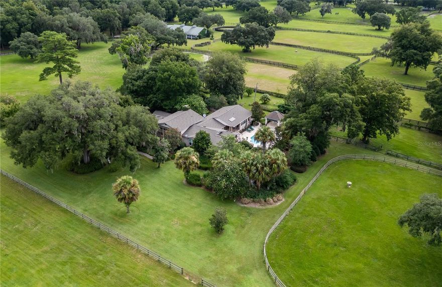 Located on a quiet country road in NW Marion County, River Mist Farm offers 42 acres of spacious pastures, glorious live oaks, and spectacular gardens and privacy. As a private horse facility the farm has been the birthplace of multiple stakes winners and champions and  
offers stunning landscape for whatever equestrian discipline you pursue. A beautiful canopy of crepe myrtles shade the driveway as it leads towards the 3-bedroom, 3-.5 bath multi-story main home built in 2005 featuring a unique layout with bamboo wood flooring and lots of natural light. There is no shortage of remarkable spaces in the home– The kitchen is fully equipped with stainless appliances including a Thermidor gas range and Sub Zero fridge, a large center island with granite countertops, lots of storage space, and an additional pantry. Adjacent to the kitchen is a lovely built-in wet bar complete with beverage fridge and direct access to the back patio. The main living area is a huge space that provides extensive built-in shelving and a wood-burning fireplace with tasteful brick facade. All bedrooms are inviting, though the primary suite is an especially notable space that showcases cathedral wood-beamed ceilings, a large layout, private access to the pool area, two large walk-in closets with comprehensive glass-front shelving units, and a private en-suite with a huge walk-in shower and dual vanities. Interesting spaces continue throughout the home, including the spacious in-house mud/laundry room with plenty of cabinet storage, a family room, multiple flex spaces including an office/den area that is home to a wine cellar and safe room, and a light and bright multi-use area that currently serves as an aviary. To the back of the home is the stunning pool area that provides the perfect place for entertaining and unwinding. A sparkling in-ground pool is adorned with a decorative rose motif, surrounded by a huge pool deck and several covered areas including a gazebo, summer kitchen space, a koi pond, a bocce court, an original antique cracker dog house, and several quiet reflecting areas within the garden. The care and dedication to the property are evident from the extensive established gardens, which bloom with perennials, agapanthus, hydrangea trees, and even angel trumpets. This property is perfect for those with a green thumb and even includes a greenhouse/garden shed with lots of natural light and plenty of space for growing potted plants all year long. A large generator, high-impact windows throughout, and a tornado closet offer additional peace of mind. Brand new roof! For equestrians a lovely 8-stall block barn features oversized stalls, barn office, bathroom, and a large loft that could be finished into a barn apartment if desired. A secondary barn is also in place, offering an additional 4-stalls, 12 paddocks, feeder pens, and a large round-pen are also established, and the farm’s great land is scattered with gorgeous granddaddy oaks for gentle shade with lots of areas to ride and train. All of this and more are located less than 10 minutes from HITS and 15 minutes from the World Equestrian Center and OBS making this a standout property for anyone looking to "Live the Ocala Dream!"