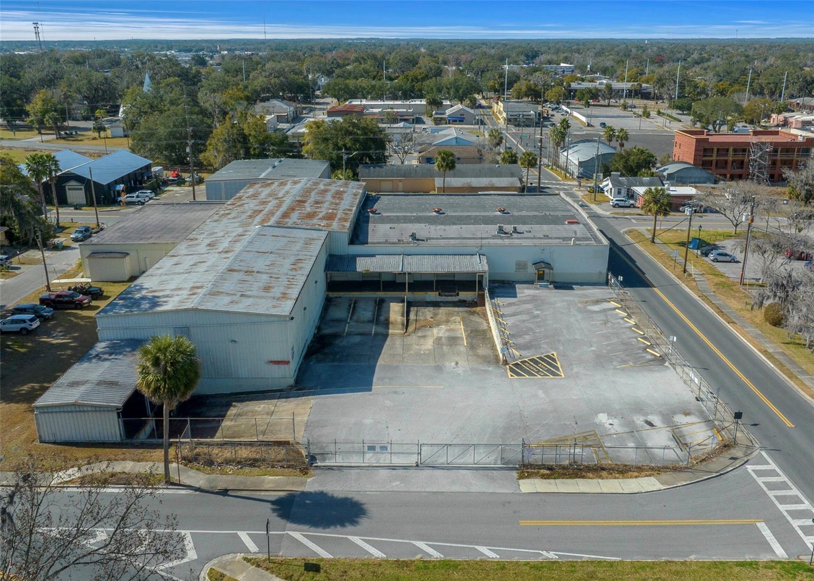 This highly desirable, oversized downtown parcel spans a full city block with street frontage on all four sides and offers a prime location in the heart of Ocala's vibrant downtown area. The 1.34-acre site is zoned FBC (Form-Based Code) and includes three buildings that are interconnected totaling over 30,120 SF under roof, plus a large covered canopy area.
Formerly the School Board of Marion County's supply warehouse, the property is equipped with all city utilities and fire sprinklers throughout. The site also features 15 paved parking spots, with additional paved areas available. Located just one block from the Downtown Market, an open-air facility that hosts regular events, and walking distance of the downtown "Square" and public parking, this parcel is an ideal location for businesses looking to capitalize on the area's explosive growth.
The surrounding downtown area is experiencing significant redevelopment, including new residential 'city living' units and numerous commercial projects for lodging, amenities, food, and shopping. With its versatile space that includes warehouse areas, offices, loading zones, and a covered canopy, this property offers endless possibilities for a wide range of uses or redevelopment opportunities.