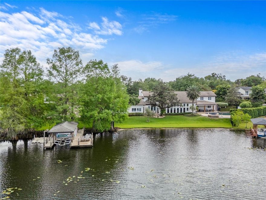 Tucked away at the end of a quiet cul-de-sac, this serene lakefront retreat is sited on a lush 1.21-acre lot w/ 187 feet of shoreline on tranquil Lake Nina—part of the Winter Park Chain of Lakes—this 4-bedroom, 4.5-bathroom, 4,997-square-foot estate blends Santa Barbara-style charm w/ modern sophistication in one of Central Florida’s most desirable settings. A meandering drive leads you to a semi-circular paver driveway that welcomes you home. A deep, covered front porch provides a gracious entry, setting the tone for the calm, understated elegance found throughout. Once inside, nearly floor-to-ceiling windows span the entire rear elevation, offering breathtaking lake views from every angle & filling the home w/ natural light. To the right of the foyer, a cozy formal living room w/ a wood-burning fireplace invites quiet conversations or evening relaxation. To the left, the spacious dining room features a built-in buffet designed to preserve unobstructed views of the water. Just beyond, the newly renovated kitchen is a standout including a La Cornue French gas range, Monogram appliances, a concrete farmhouse sink, wide-plank oak flooring, luxury lighting & striking marble counters. A hidden scullery/laundry area offers practical overflow, connecting the kitchen to the oversized, air-conditioned 2-car, side-facing garage w/ built-in storage & a dedicated gym or flex room. Moving through the heart of the home, a large family room awaits—framed by soaring ceilings with cedar beam accents & outfitted w/ automated shades for comfort & privacy. The primary suite occupies its own wing & features a gas fireplace, dual walk-in closets, a spa-style bath, & 2 separate flex rooms currently used as an office & art studio. On the opposite side of the home, a tucked-away powder bath conveniently serves both guests & the pool area, while an additional en-suite bedroom downstairs offers privacy for guests or multi-generational living. Upstairs, two more bedrooms w/ en suite baths flank a generous loft w/ amazing lake views. Step outside & the setting is nothing short of spectacular. The resort-style backyard was designed for entertaining & unwinding alike, w/ multiple fire pits, a sparkling pool & raised spa & an outdoor kitchen complete with grill, pizza oven, built-in space for Green Egg, sink & refrigerator. The expansive lawn gently slopes toward the lake, leading to a rare, fully outfitted dock w/ a covered boathouse, lift, dual jet ski slips & utilities for water & electric—perfect for sunset cocktails or launching into the larger chain of lakes. Architectural details throughout the home include Mexican tile, natural wood & stone finishes, vaulted ceilings, metal accents, & custom lighting—thoughtfully layered to create a warm & inviting atmosphere. Major improvements include a home repipe (2020), updated electrical (2019), 3 new HVAC systems (2022), new garage doors (2021), & recently installed paver hardscape designed to accommodate ample parking for family & guests. In a sought-after Maitland lakefront enclave, this home pairs top schools w/ rare privacy & convenience. Lake Nina provides a quiet, scenic backdrop, yet a short, easily navigable canal offers direct access to the expansive waters of Lake Maitland & the greater Winter Park Chain—making it as ideal for tranquil mornings as it is for adventurous afternoons on the water. More than a home, this property is a lifestyle, a legacy & a front-row seat to the best of lakefront living.