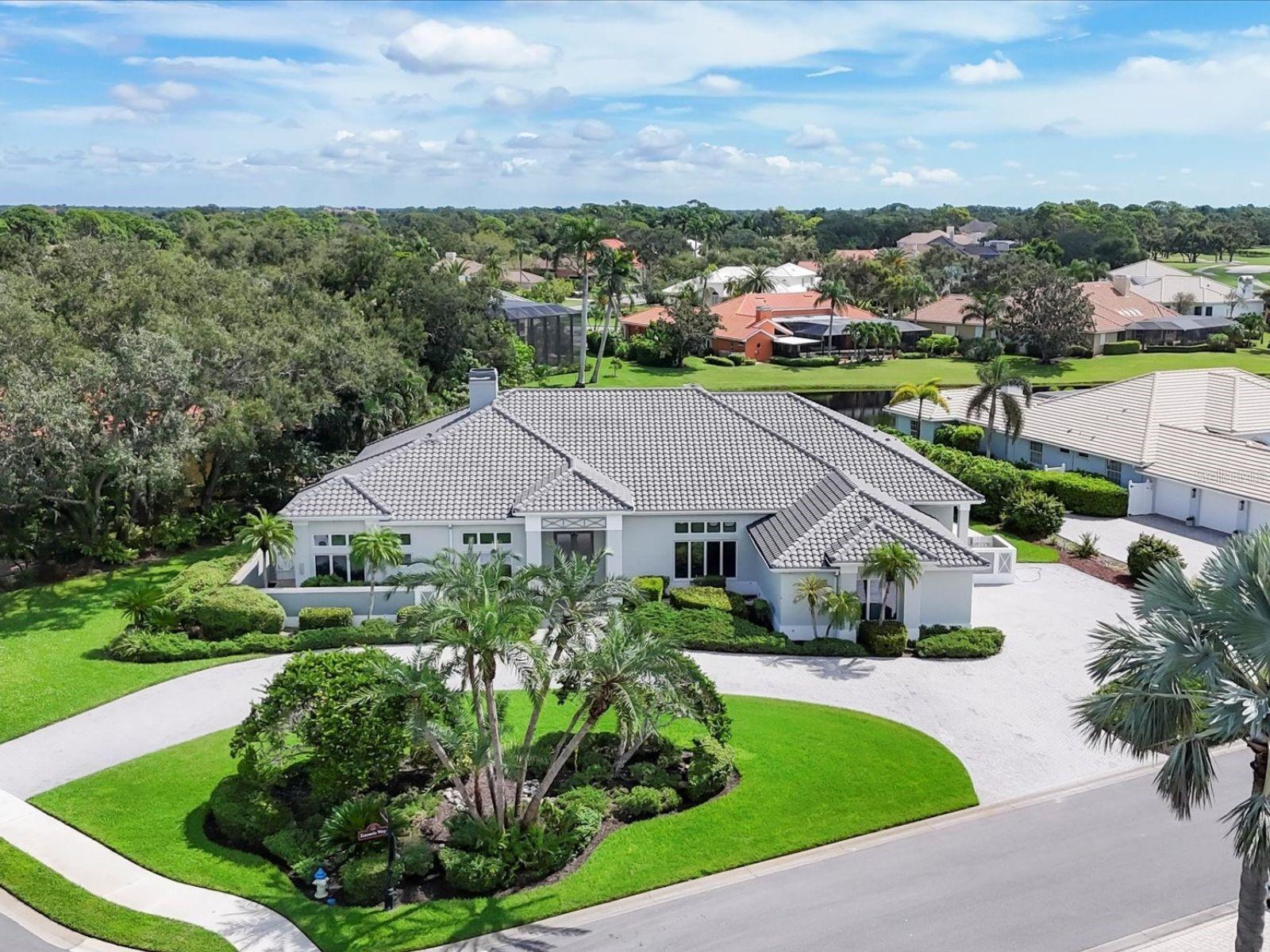 Set on a serene half-acre homesite in Prestancia, this single-story residence combines timeless architecture with a floor plan designed for both elegance and ease. A circular paver drive framed by manicured lawns, tropical palms, and a landscaped center island leads to a crisp, bright front elevation recently enhanced by a new roof completed in 2024. Wide steps and column accents mark the approach to a grand double-door entry, where soaring ceilings and abundant natural light immediately set the tone. Throughout the home, nearly every room is graced with transom windows, volume ceilings, and smooth-finish surfaces creating an airy, light-filled environment. The heart of the home is its expansive great room, anchored by a stone fireplace and complemented by a custom entertainment wall, a built-in bar, and generous shelving, an ideal space for gatherings and everyday relaxation. Pocketing glass doors open to the lanai, where covered dining and lounge areas flow seamlessly to the screened pool terrace. Here, a sparkling pool with a raised fountain and cascading water feature creates a tranquil backdrop, surrounded by lush landscaping. The kitchen offers generous refrigeration capacity, double ovens, abundant cabinetry, and a built-in desk station, ensuring both function and opportunity for future customization. A breakfast nook with cabinetry opens directly to the lanai, making casual meals feel like part of the indoor-outdoor experience. The private primary suite is a true retreat, offering soaring ceilings, space for a sitting area, direct lanai access, and a well-appointed office with garden views, situated for privacy and convenience. The spa-inspired bath includes dual vanities, a makeup counter, a soaking tub, and a curved walk-in shower with dual showerheads. Two guest suites with ensuite baths provide comfort for family or visitors, one of which also serves as a pool bath. A powder bath just off the foyer, a well-appointed laundry room, and a side-entry garage complete the layout. With 4,131 square feet of living space, this 3-bedroom, 3.5-bath home balances comfort and entertaining within one of Sarasota’s most prestigious gated golf course communities. In Prestancia, residents enjoy optional TPC memberships with golf and social opportunities, plus convenient access to The Legacy Trail, Siesta Key Beach, downtown Sarasota, St. Armands Circle, and the barrier islands.