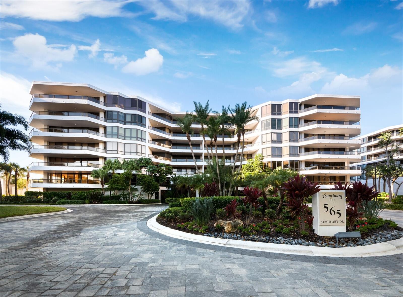 Nestled behind the exclusive gates of the Longboat Key Club, The Sanctuary enjoys an enviable location along a pristine stretch of Longboat Key’s Gulf beach. This exceptionally renovated 3BR, 2.5BA residence with nearly 2,400 square feet of living space is simply stunning. This corner residence features a thoughtful split-bedroom layout, elegant finishes and floor to ceiling high-impact glass leading to an open, wraparound terrace, where views of tropical palms and lush green space set the tone for outdoor dining, entertaining or a peaceful retreat. Inside, neutral tones with tasteful accents combine with walls of glass to create a bright, flowing ambiance. Trey ceilings, engineered hardwood flooring and tile in the baths add refined detail. The oversized kitchen is exceptional, with colorful cabinetry, stone countertops, and a large island with breakfast bar seating that opens seamlessly to the living room. Residents of the Sanctuary enjoy a recreational room, 24hr security guard, heated swimming pool, 2 Har-Tru tennis courts, and on-site management. Just steps away, the exclusive Longboat Key Club offers championship golf, a deep-water marina, a world-class spa, a private beach club, and fine dining, providing an unparalleled coastal lifestyle.