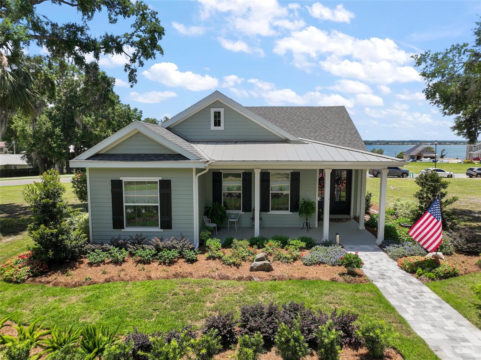 Welcome to 622 W 11th Avenue, a stunning 2024 custom-built home by Kevco Builders located in the highly desirable Cottages on 11th neighborhood in historic Mount Dora. This thoughtfully designed residence combines timeless charm with modern luxury and is just blocks from downtown shops, restaurants, parks, and the Lake Dora waterfront. From the moment you arrive, you'll be captivated by the home’s inviting curb appeal, accent metal roof, shutters, flagstone walkway, professional landscaping, and peaceful lake views beyond. Step inside to discover a beautifully appointed interior featuring crown molding throughout, solid core doors, 3" trim and return molding on all windows, and laminate wood flooring throughout. The open concept living area is anchored by a custom stone fireplace with gas logs and barn doors add a touch of farmhouse elegance to both the living room and owner’s suite. The gourmet kitchen showcases custom cabinetry, quartz countertops, a subway tile backsplash in a herringbone pattern, Thermador stainless steel appliances, gas cooktop, farmhouse sink, center island and decorator lighting. The owner's suite is a peaceful retreat with shiplap detailing, a spa-style bath with glass barn door shower enclosure, garden tub, double vanity with custom cabinets & custom mirrors and large walk in closet. The second bath is equally stylish with additional shiplap, walk in shower and high-end finishes. Designer-selected woven wood blinds are installed throughout the home, and the laundry area includes a full-size LG washer and dryer combination unit for added convenience. Exterior features include energy-efficient spray foam attic insulation, MI Energy Efficient Impact Windows, gas tankless hot water heater, seamless gutters, paver driveway and walkways, an acrylic-finished front porch and rear lanai, and an epoxy-coated garage floor. The garage also comes equipped with a Gladiator cabinet and tool organization system. Irrigation and professional landscaping complete this move-in-ready home. Whether you’re enjoying a quiet morning on the porch or entertaining friends on the covered lanai, this home offers the perfect blend of comfort, efficiency, and style in one of Mount Dora’s most walkable and charming communities.