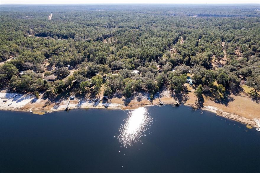 This lakefront retreat on Mason Lake offers the perfect balance of natural beauty, tranquility, and modern comfort. Situated on a gorgeous wooded lot surrounded by majestic oaks and longleaf pines, the 2014-built home feels like a private escape while delivering the conveniences of contemporary living.
The thoughtfully designed layout centers around a custom kitchen that anchors the open living and dining spaces, ideal for both everyday living and entertaining!   A cozy wood-burning fireplace creates a welcoming gathering spot, while three spacious bedrooms—each with its own private ensuite bath—offer exceptional comfort, privacy, and flexibility for family and guests.  Step outside to the screened lanai, generous enough to host a crowd yet perfectly suited for intimate evenings. With panoramic lake views and seamless indoor–outdoor flow, this inviting space can be enjoyed year-round!  Outdoor living continues with a charming brick fire pit for evening gatherings, complemented by a lakeshore covered deck that provides shaded seating and direct access to the water. An oversized outdoor shower offers a refreshing rinse after long days on the lake.  Mason Lake is ideal for water sports, including boating, kayaking, paddle boarding, tubing, and swimming in its clear, refreshing waters.  Located just 30 minutes from Gainesville, this Lake property offers easy access to shopping, dining, and the University of Florida—while remaining far enough away to preserve true lakeside peace!  Beautifully maintained and thoughtfully designed, this modern lakefront retreat combines comfort, privacy, and recreation.  This is a rare opportunity—schedule your private tour today.