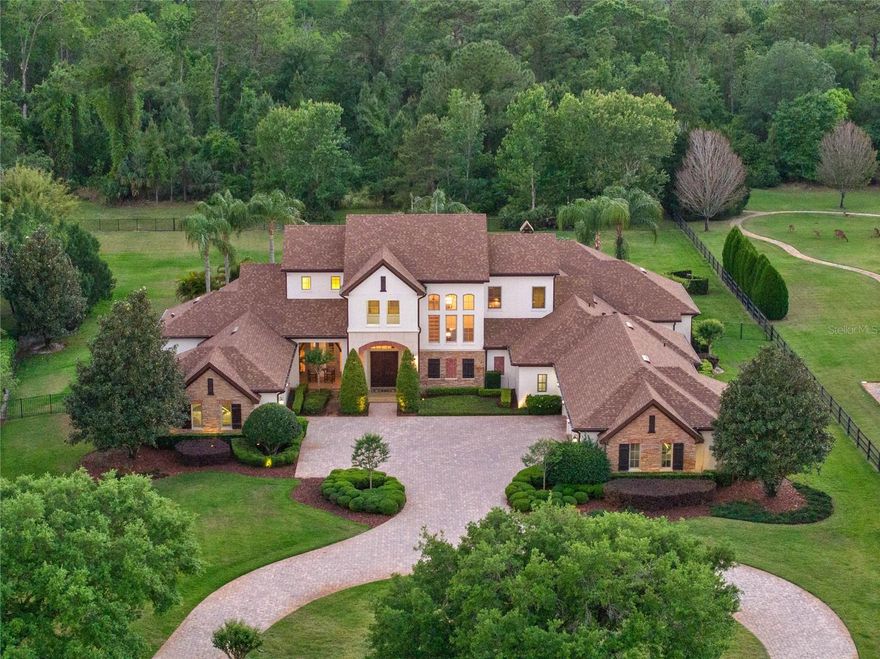 Welcome to this exceptional custom-built estate in the gated community of Mills Cove, where timeless luxury meets relaxed Florida elegance. Tucked away on 1.28 acres, this meticulously designed home spans over 6,100 square feet of refined living space, thoughtfully crafted for grand entertaining and everyday comfort. Car enthusiasts will appreciate the oversized four-car garage and extended driveway, ideal for showcasing your collection with ease and style! Step through the grand double doors into an expansive sunlit foyer, where soaring ceilings and classic architectural details set the tone for the home’s sophisticated design. At the heart of the home, the gourmet kitchen features high-end appliances, a generous center island, an adjacent butler's pantry, complete with wet bar, wonderful for effortless entertaining. Just beyond, discover a cleverly tucked away wine room beneath the staircase, complete with a hidden room designed to showcase and secure your most prized vintages, a collector's dream. Disappearing pocket sliding doors offer seamless indoor-outdoor living, opening to expansive patios that frame a resort-style pool and spa, summer kitchen, outdoor fireplace and tranquil lake views, your private oasis for gathering or unwinding. The primary suite is a retreat, thoughtfully positioned for privacy and featuring a spa-inspired bath, a jaw-dropping custom closet and private garage access directly from the suite, an extraordinary touch for those who value discretion and design. A main-level guest suite offers comfort and privacy for visitors, while upstairs, three additional bedrooms with en suites, each with walk-in closets, provide luxurious accommodations. The home also features dual laundry rooms, one on each floor, a detail that sets this property apart in functionality and ease. Just off the main living area, the executive office offers functionality and inspiration, featuring serene views of the pool and private outdoor access, ideal for focused workdays or taking client calls with a resort-style backdrop. The billiards/theater room boasts full home cinema seating, a large screen, and rich finishes that make it the ultimate space for movie nights or game day gatherings. Ideally just minutes from Lake Pickett and best of Oviedo’s shops, and dining, this extraordinary residence delivers a blend of elegance, privacy and sophistication. Don't miss your opportunity to own one of Central Florida's stunning custom estates. Schedule your private tour today.