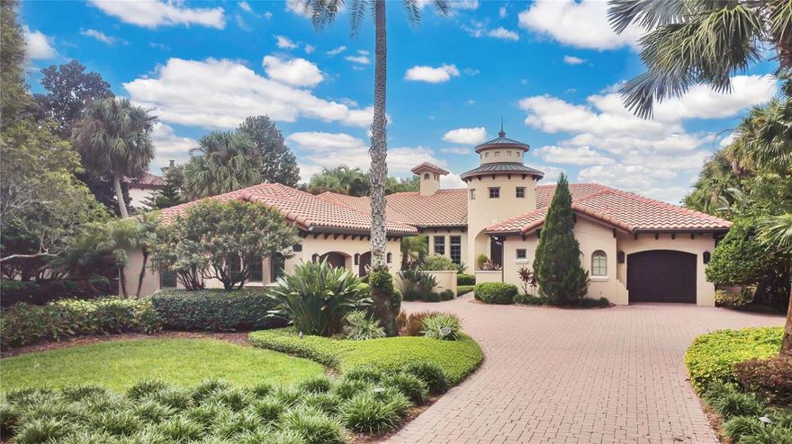 Experience the art of fine living in this exquisite one-story Modern Mediterranean garden villa, offered fully furnished with a curated designer furniture package. Every detail has been thoughtfully crafted, blending timeless architecture with refined finishes and effortless comfort.
Inside, travertine floors, wood-beamed ceilings, and solid wood doors set a warm, sophisticated tone. Custom cabinetry, designer window treatments, and rich textures throughout create a sense of understated luxury. The double island kitchen is a culinary masterpiece, featuring Quartzite countertops, a marble mosaic backsplash, gourmet appliances, a gas stove, wet bar, and butler’s pantry—perfect for both intimate dining and grand entertaining. 
A cast stone fireplace anchors the elegant living room, while the expansive family room opens through panoramic sliding doors to a covered lanai, creating a seamless indoor-outdoor experience.
The primary suite is a sanctuary of indulgence, complete with a morning bar, private sitting area, spa-inspired bath, and generous walk-in closet. A wood-floored study with custom built-ins provides a refined space for work or reflection.
Outdoors, the resort-style setting is framed by lush tropical landscaping and tranquil pond views. The spacious lanai features a summer kitchen and pool bath overlooking a heated saltwater pool and spa—your private oasis for relaxation and entertaining. A three-car garage completes this extraordinary residence, where every element has been designed for the most discerning homeowner. Isleworth is surrounded by the Butler Chain of Lakes and known for its manicured gardens, timeless architecture, and unparalleled privacy. This exclusive guard-gated community offers 24-hour security and the opportunity to join the Isleworth Golf & Country Club featuring world-class golf, tennis, resort-style pool, fitness, dining, and social events. Garden Villas include exterior grounds maintenance for effortless living.