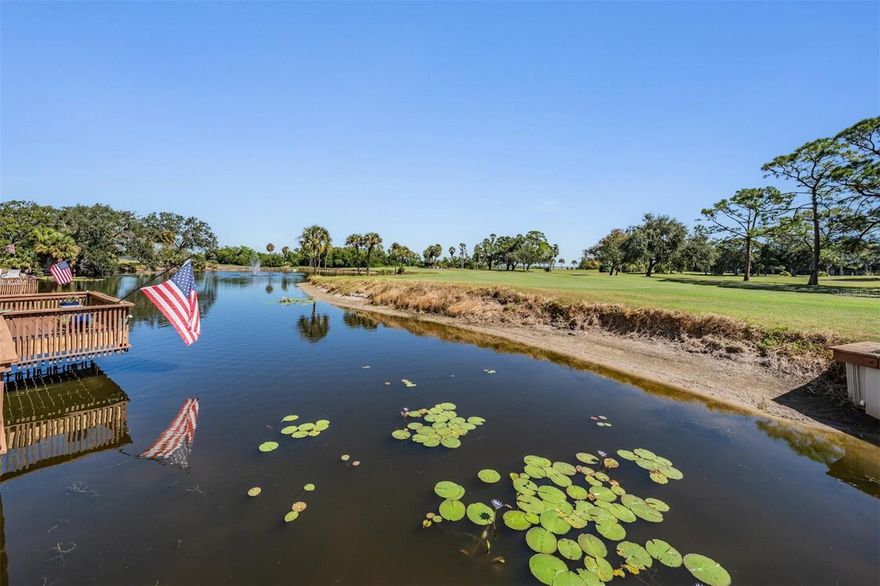 Welcome to one of Cove Cay’s coveted seven condos with an oversized outdoor deck—set above a tranquil pond on the 15th hole—where bay breezes and ever-changing views of water, wildlife, sunrises, and golfers become your daily backdrop. The 16' x 13' deck (208 sq. ft.) was rebuilt in 2025 with composite Trex for beauty, durability, and years of low-maintenance living. Wide PGT impact sliders open to a screened porch that flows out to the deck—hello, indoor-outdoor entertaining.  Inside, the open kitchen is light and bright, featuring a double PGT impact window, white soft-close cabinetry, exquisite light granite with neutral veining that doubles as an expansive serving/snack bar, a ceiling detail with crown moulding and integrated lighting, stainless appliances, a deep stainless undermount sink with a sleek black gooseneck faucet, decorative backsplash, and a dedicated coffee bar. Pergo DuraCraft waterproof luxury vinyl plank runs throughout for cool comfort, easy care, and long-term durability. Fresh, airy wall colors elevate the spacious living/dining area, which includes an attractive built-in and the perfect wall for a large TV. The serene primary suite enjoys PGT windows framing the pond and golf course. Its en-suite bath offers a large vanity, distinctive lighting, updated tile shower and flooring, and a custom walk-in closet. The second bedroom flexes beautifully as a den, office, or guest room, and the refreshed hall bath is another win.  Practical perks abound: a 2023 Trane A/C, a newer water heater, hurricane windows throughout and your own private laundry room just steps from the front door with full-size washer/dryer, storage cabinet, and high shelving. This corner residence adds privacy and sits just moments from the Village 2 pool and recreation area—as well as your carport.  Lush landscaping, shimmering water and fairway vistas, 24/7 security, and well-kept amenities make this the paradise known as Cove Cay.