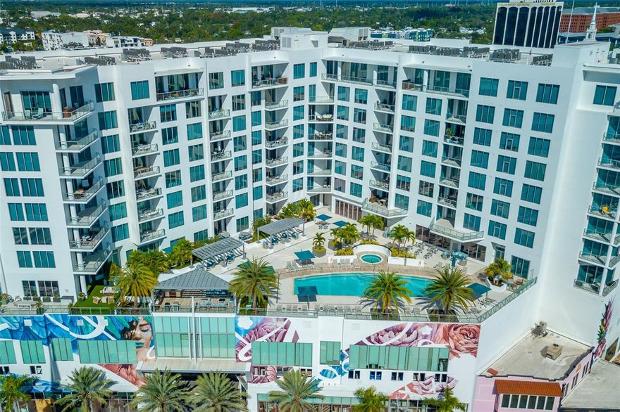 Experience an elevated expression of downtown Sarasota luxury at Residence 1013 in Mark Sarasota, where contemporary elegance meets resort-style sophistication. Positioned on the highly sought-after tenth floor—regarded as one of the building’s most distinguished residential levels—this residence offers a refined sense of exclusivity shared by its discerning residents. Located in the heart of Sarasota’s most dynamic cultural and coastal district, this exceptional home embodies modern design, subtle comfort, and the vibrant convenience of downtown living. The split floor plan features two bedrooms plus a den and two-and-a-half baths, spanning 1,577 heated square feet and 1,711 total square feet, including a covered terrace, optimally square in design, providing defined depth and width. The expansive outdoor living space feels secluded yet connected— nestled among lush treetops with park-like views of Smithsonian-registered Mermaid Fountain in nearby Paul Thorpe Park, formerly known as Pineapple Park, offering shaded seating. Enjoy distant southern city vistas, westerly views of the tropical pool deck and glowing Sarasota Bay sunsets. The open-concept layout highlights soaring ceilings, floor-to-ceiling glass, 10-foot ceilings, distinctive, architectural grand-format porcelain tile flooring with a textured finish and exquisite designer finishes. A gourmet kitchen showcases an upgraded induction cooktop for fast, energy efficient cooking, imported custom cabinetry, stone countertops, a bespoke backsplash and premium stainless-steel appliances—flowing effortlessly into radiant living and dining areas ideal for entertaining or quiet reflection. The southern-facing living room enjoys tranquil natural light without the need for shades and each bedroom adorns top-tier Silhouette blinds. The south and southwest orientation provides privacy, protection from wind and rain, as well as a quiet and serene ambiance. The primary ensuite serves as a peaceful sanctuary with a spa-inspired bath, electrified mirrors with custom lighting, a spacious walk-in closet and a door that opens to direct terrace access. Two deeded VIP parking spaces, fully covered, centrally located, protected from the elements and are located just steps from the elevator. A generous climate-controlled storage unit in a secure room—where packages are safely held—adds exceptional convenience only steps down the hall. The fifth-floor amenity deck crowns Mark Sarasota with resort-style indulgence: a heated saltwater infinity pool, spa, fire-pit lounge, grilling pavilion, bar, club room with catering kitchen, billiards, newsroom,  a premier fitness center with yoga and spin studios equipped for virtual workouts. Beyond your door, experience the best of downtown Sarasota—from fine dining at Hyde Park Steakhouse, State Street Eating House, for more casual fare, Boca or Besos for tapas, to evenings at Sugar, Sarasota’s glamorous piano and champagne bar. Explore nearby luxury car dealership, galleries, salons, smoothies at Toastique, Bodybar Pilates and Ride Cycling Studio. Cultural treasures such as the Sarasota Opera House, Florida Studio Theatre, and Sarasota Art Museum are walking distance, while boaters will enjoy Marina Jack. Lido Beach is over the Ringling Bridge. With 24-hour concierge service, secure access, on-site management and a pet-friendly atmosphere, effortless grandeur unites luxury, convenience and Sarasota’s signature coastal charm in one unforgettable downtown address.