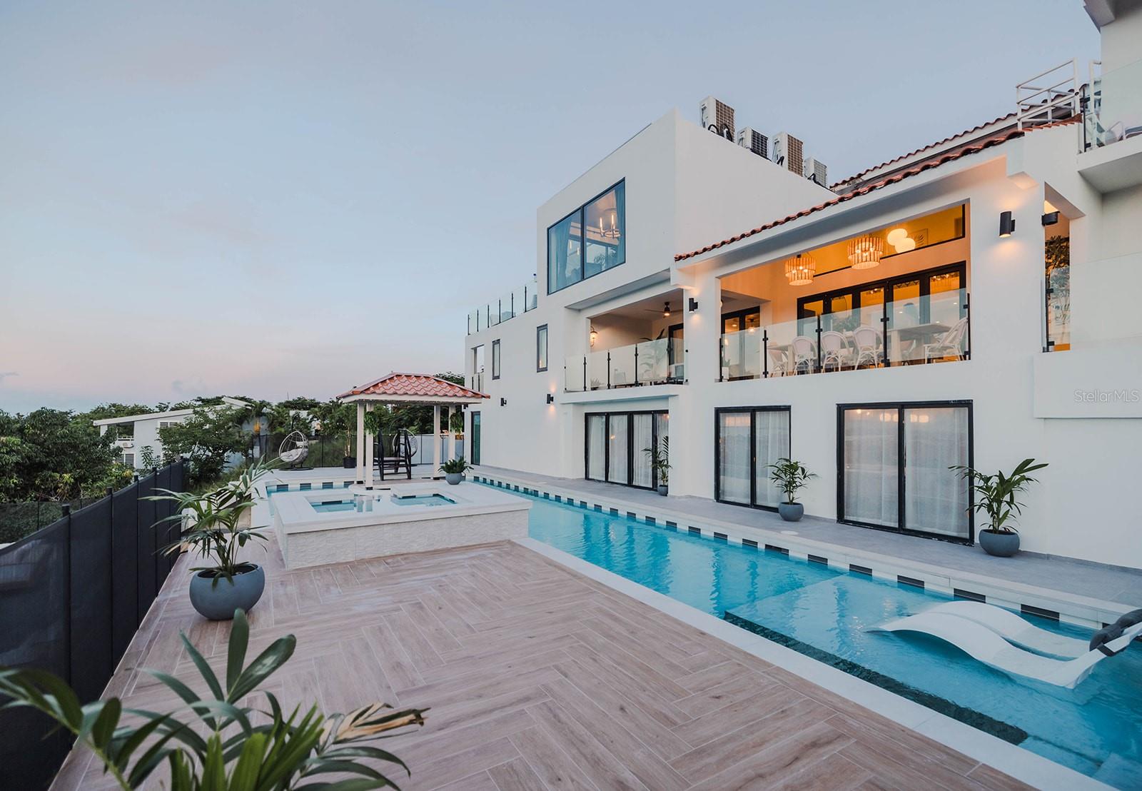 Offered Fully Furnished | 7 Beds | 8 Baths | Office | Library | Theater | Pool | 8,682 SF Interior | 4,000+ SF Outdoor Living | 1.10 Acres
Welcome to a rare opportunity to own one of the most extraordinary luxury estates in Palmas del Mar, Puerto Rico’s premier resort community. Located on two buildable parcels totaling 1.10 acres, this fully furnished and professionally designed residence is a masterpiece of architecture, technology, and lifestyle living. This property was expanded and renovated for three years, and it was finished in 2024.
Impeccably Designed Living:
Spanning 8,682 SF of air-conditioned interiors, the home showcases custom-built cabinetry, imported furniture, designer lighting, and high-end appliances throughout. Each space has been curated to perfection, from the elegant primary suite with a fire-pit balcony and spa-like bathroom to the private library, executive office, and media den.
Ultimate Entertainment Level:
Entertain with ease in a dedicated level featuring a poker lounge, second kitchen, climate-controlled wine cellar, 130” 4K Dolby Atmos home theater, game room, and an impressive 5-bed bunk suite designed for guests or multi-generational living.
Resort-Style Pool Complex:
Step into your personal oasis with a resort-style pool, spa, lazy river, and swim-up bar — all framed by over 4,000 SF of covered outdoor patios and balconies designed for year-round enjoyment.
State-of-the-Art Kitchen:
The chef’s kitchen features Gaggenau appliances, a hidden air-conditioned walk-in pantry, and surge-protected electrical panels for maximum protection and performance.
Tech-Forward & Resilient:
Equipped for modern living with a 63-panel, 30 kW solar system, whole-home generator, CAT-6 mesh network, dual-ISP failover, AI security system, and hurricane-rated 2025 windows throughout. Climate comfort is assured with a new high-efficiency HVAC system and programmed landscape lighting.
Detached Guest Studio:
A separate, fully air-conditioned studio with full bath is ideal for a home gym, in-law suite, living-nanny suite, creative space, homeschool pod, or remote office.
Future Expansion:
The second parcel is prepped for a guest villa, car pavilion, or additional structure, without altering the current driveway or layout.
HOA dues: $2,000/year (approx. $1,000/lot)
Shown by private appointment only. Proof of funds required
