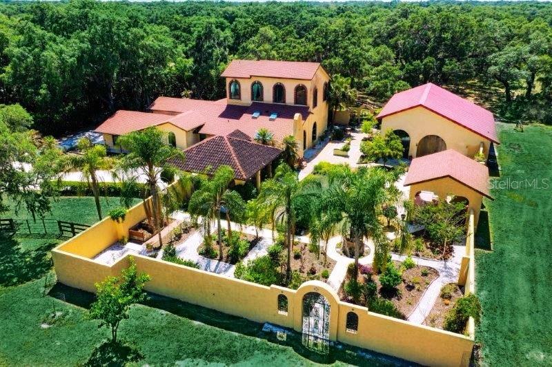 Welcome to this spectacular estate on over 5 acres in the popular equestrian community of Saddle Creek! This unique 2 story Spanish Mediterranean home has been meticulously updated with a European flair with a portico, cabana, covered porch and walled garden/courtyard filled with flowering trees and tropical plants. A stunning masterpiece it is the perfect blend of peace and tranquility with canopied oaks, mature trees and a natural pond. The home itself boasts over 4000 SF under air with 4 bedrooms, 3 baths plus a den. As you enter this spectacular home the kitchen features gorgeous custom cabinets and quartz counters with a center island, newer stainless appliances, and a huge walk in pantry. The formal dining area is perfect for large gatherings with an area for a wine wall/closet with ornate iron accents. The spacious living room includes a decorative Victorian fireplace with lighted custom niches, surround sound and recessed lighting. There are french doors to the beautifully tiled screened lanai with a spiral staircase leading to the upstairs patio. Retire to your impressive master suite with bamboo floors and the huge balcony overlooking the canopied oak trees. The master bath features his and her vanities with pedestal tub, separate water closet and bidet and large tiled shower. The impressive his and her walk in custom designed California closets will impress you and have ample room for storage as well. The first floor bedrooms are spacious with walk in closets and the baths are tastefully updated with new vanities, tile and fixtures. There is also a large storage room as well as laundry room with cabinets. Careful and thoughtful detail has gone into the thorough remodeling of this home in 2018/2019 which includes new roof, 3 A/C's, new hurricane impact windows, new plumbing and electrical and freshly painted inside with new floors throughout. All buildings have been spray foam insulated which means extremely energy efficient. New well equipment and Culligan water treatment system have been installed as well as reverse osmosis for drinking water. The barn itself includes over 2100SF with an air conditioned artist studio and machine shop and room for plenty of stalls for horses or the car enthusiast. The walled courtyard which joins the home and barn with portico and cabana was inspired by an English estate garden and is filled with shell paths around the desert garden and fruit trees. The entire property is fenced and perfect for horses and there's plenty of room for a pool. This estate encompasses over 8900 SF of living space so whether you are a garden enthusiast, equestrian rider, artist or even car collector this home has it all! Conveniently located yet away from the hustle and bustle and near A-rated schools, Siesta Beach, shopping and restaurants. It truly is a one of a kind estate!