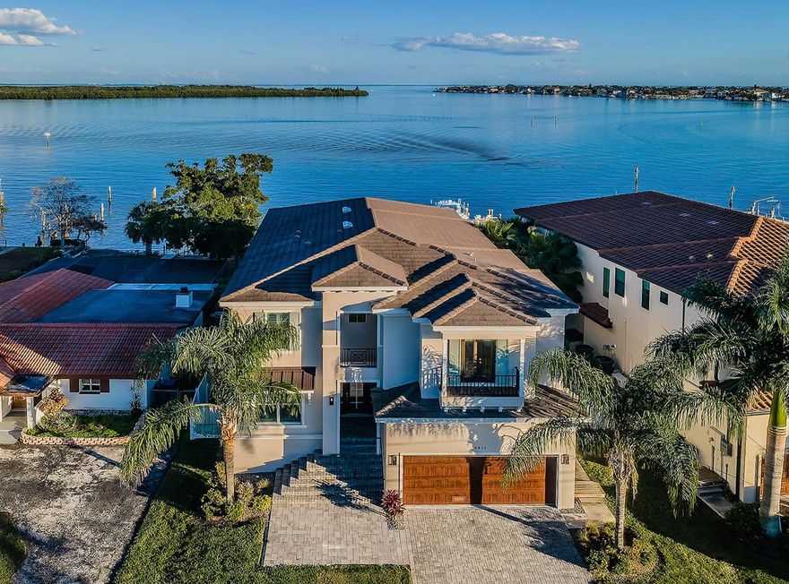 STUNNING OPEN WATER VIEWS ARE YOURS FROM THIS LUXURIOUS 5 BEDROOM, 5 BATH, COASTAL CONTEMPORARY ESTATE RESIDENCE - CLOSE TO EXCEPTIONAL SCHOOLS, DINING, SHOPPING AND GOLF!  Built in 2019 on a deep waterfront lot, you’ll love the high ceilings, exquisite driftwood-stype porcelain floors, gorgeous woodworking and remarkable attention to detail.  Your welcoming entry foyer opens to a cavernous greatroom-plan with spectacular waterviews.  Superb gourmet kitchen boasts fine quartz counters, modern-motif wood cabinetry, gas cooking, stainless steel Viking Appliances, a large center island bar with farmhouse sink and seating for five, extensive storage with pull-out organizers, and a sizable walk-in pantry.  Spacious waterfront dining is complemented by a grand living room that opens to a terrific 36ft-wide, 500sqft covered entertainment balcony with fully built-in luxury kitchen/gas cooking center, and access to a lavish full-size pool bath.  Sliding glass doors pocket between living room and balcony - creating a fabulous indoor-outdoor living experience.  1st living level provides a large guest bedroom suite with an exquisite private bath.  Upstairs, you’ll be greeted by an oversized 350 sqft entertainment common area that opens to a large covered balcony with commanding views of the waterfront.  Double doors introduce the impressive owners suite with beautiful waterviews, private access to the waterfront balcony, and two large walk-in closets with closet systems.  Sumptuous owner’s bath is a posh, pampering escape, with two richly-finished vanities, a fine soaking tub, and a dazzling multi-head walk-in shower.  All bedrooms are oversized and have walk-in closets, and all baths are luxuriant. Step out back and discover a private, inspiring waterfront oasis.  Large paver deck with extensive seating/lounging, encases a splendid Pebbletec pool and elevated hot tub.  Artificial turf includes a putting green area.  Updated seawall supports a superior composite dock with lighting, dedicated shower, stainless steel wire handrail guides and a 7,000lb boat lift configured for 2 jet skis.  Numerous updates/upgrades include instant hot water heating, PVC privacy fencing, pre-plumbing for upper and lower level laundries, pre-built for elevator, 3-car garage parking with 13ft-high ceilings (potential for elevated storage), and much more....Flood insurance if $550 / year.