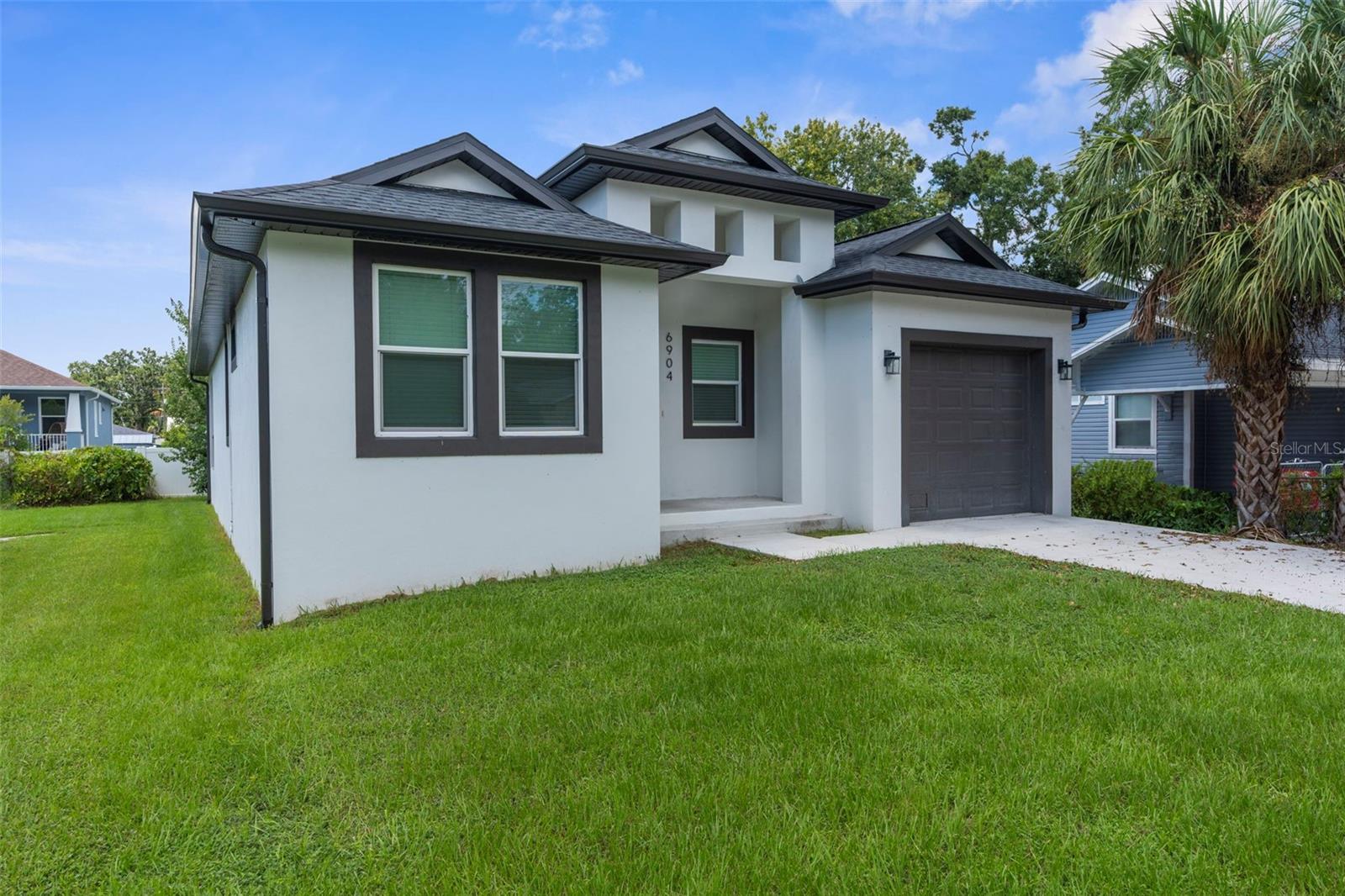 6904 N Lynn Ave offers nearly new construction in the heart of Seminole Heights, built in 2023 and designed with just under 1,800 square feet of comfortable, modern living. The interior is finished with large-format concrete-look tile throughout—no carpet anywhere—and elevated ceilings that give the space an open, airy feel. At the center of the home, the kitchen ties everything together with shaker cabinetry, stone counters, stainless appliances, and a functional island perfect for food prep or serving guests. The kitchen overlooks the dining and living areas with a tray ceiling detail, and together they open directly to the oversized covered lanai, creating an easy indoor-outdoor flow. The lanai is large enough for both a dining table and a lounge setup, ideal for year-round entertaining.
The primary suite features another tray ceiling, a generous walk-in closet, and a well-appointed en-suite bathroom with double vanities and a frameless glass walk-in shower finished in vibrant blue subway tile laid in a staggered pattern. Three additional bedrooms are light-filled and flexible, supported by a second full bath. A laundry room, one-car garage, and a long driveway that provides extra parking round out the home’s practical touches.
Living here means you’re within easy reach of Seminole Heights favorites—morning coffee at LPCX Café, barbecue at Wicked Oak, or a dinner out at Rooster & The Till. For a more casual night, Front Porch & Bart’s Tavern is just around the corner. The Seminole Heights Garden Center offers a quiet green escape, and Downtown Tampa is only minutes away with the Riverwalk, museums, and dining along the water.