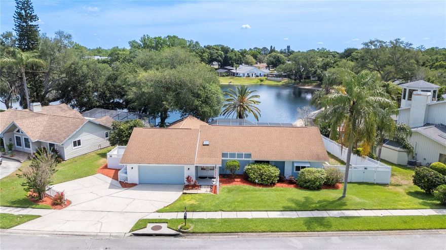 Experience the rare intersection of refined Florida living and true lakefront tranquility at 5000 Lake Valencia Blvd W in Palm Harbor. Perfectly positioned along the serene waters of Lake Valencia, this residence offers 92 feet of private waterfront frontage on a 0.28-acre homesite, delivering a setting that is both peaceful and exceptionally private.

This single-story single-family residence features 3 bedrooms, 2 bathrooms, and 1,974 square feet of thoughtfully designed living space. Inside, the home is defined by an open and airy floorplan enhanced by vaulted ceilings, skylights, and an abundance of natural light.

The kitchen serves as a central gathering space, complete with solid wood cabinetry, stone countertops, and a full suite of appliances designed for both functionality and everyday comfort. Living and dining areas flow seamlessly together, creating an effortless layout ideal for both entertaining and relaxed living.

Interior finishes include luxury vinyl and tile flooring, a split-bedroom design, and thoughtful upgrades such as ceiling fans, window treatments, and a combination kitchen/family room concept.

The outdoor living experience is anchored by a private in-ground fiberglass pool featuring a deck, lighting, and child safety fencing, all surrounded by landscaped grounds, vinyl fencing, and tranquil water and wooded views. Covered patios, a front porch, and sliding glass doors extend the living space outdoors, enhancing the connection to the natural surroundings.

Additional highlights include a security system, irrigation system, generator capability, and enhanced HVAC filtration systems.

A rare opportunity to own true lakefront property in Palm Harbor—combining natural beauty, privacy, and everyday livability on Lake Valencia.