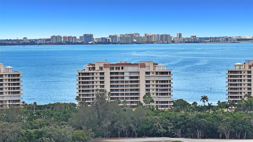 This sought-after 2,550 sq. ft. Cayman model in Grand Bay is located within the community’s desirable Building III and ideally positioned to capture magnificent Sarasota Bay and sparkling city views, with additional vistas overlooking the Harbourside Golf Course. Approximately 700 square feet of outdoor living includes two expansive terraces: an east-facing for breathtaking sunrises over the bay and a west-facing showcasing unforgettable glowing sunsets.  A private elevator foyer opens to the spacious living area with 9-foot ceilings and immediate “wow” views of the bay. The primary suite is thoughtfully positioned for privacy, featuring serene bay views, a sliding glass door to the bayfront terrace, and an updated primary bathroom with dual bath areas. The guest bedroom is located on the west side of the residence with direct access to the west-facing terrace. The den, considered an occasional 3rd bedroom, offers exceptional flexibility with two sets of concealed movable doors allowing this space to be closed off from the kitchen and dining areas for privacy, and it enjoys access to a third full bath. The dining room is centrally located, enhancing the open flow between living spaces while offering both bay and west-exposure views. The kitchen includes a breakfast room and abundant cabinetry. Luxury vinyl flooring runs throughout the residence. The condominium is being sold partially furnished for the new owner to begin their coastal journey with ease. Grand Bay residents enjoy an exceptional array of resort-style amenities, including two heated pools & spas, two Har-Tru tennis courts, a state-of-the-art fitness center with sauna, 24-hour guard-gated security, and on-site management. Miles of sidewalks and trails wind throughout the natural beauty of Bay Isles, a true sanctuary for nature lovers. Bay Isles Beach Club membership is included exclusively for owners, offering gated parking and private beach access with beach amenities, grills, and conveniences. Optional Longboat Key Club membership, including golf, is also available.